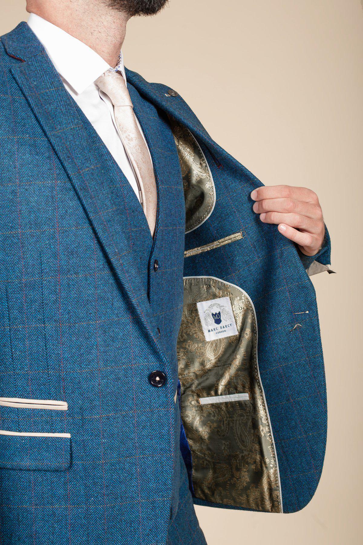 A man showcases the marcdarcy DION Blue Tweed Check Suit with Kelvin Cream Waistcoat, holding open his jacket to reveal a gold patterned lining and visible label. The elegant look is ideal as a wedding suit, with his head out of view.