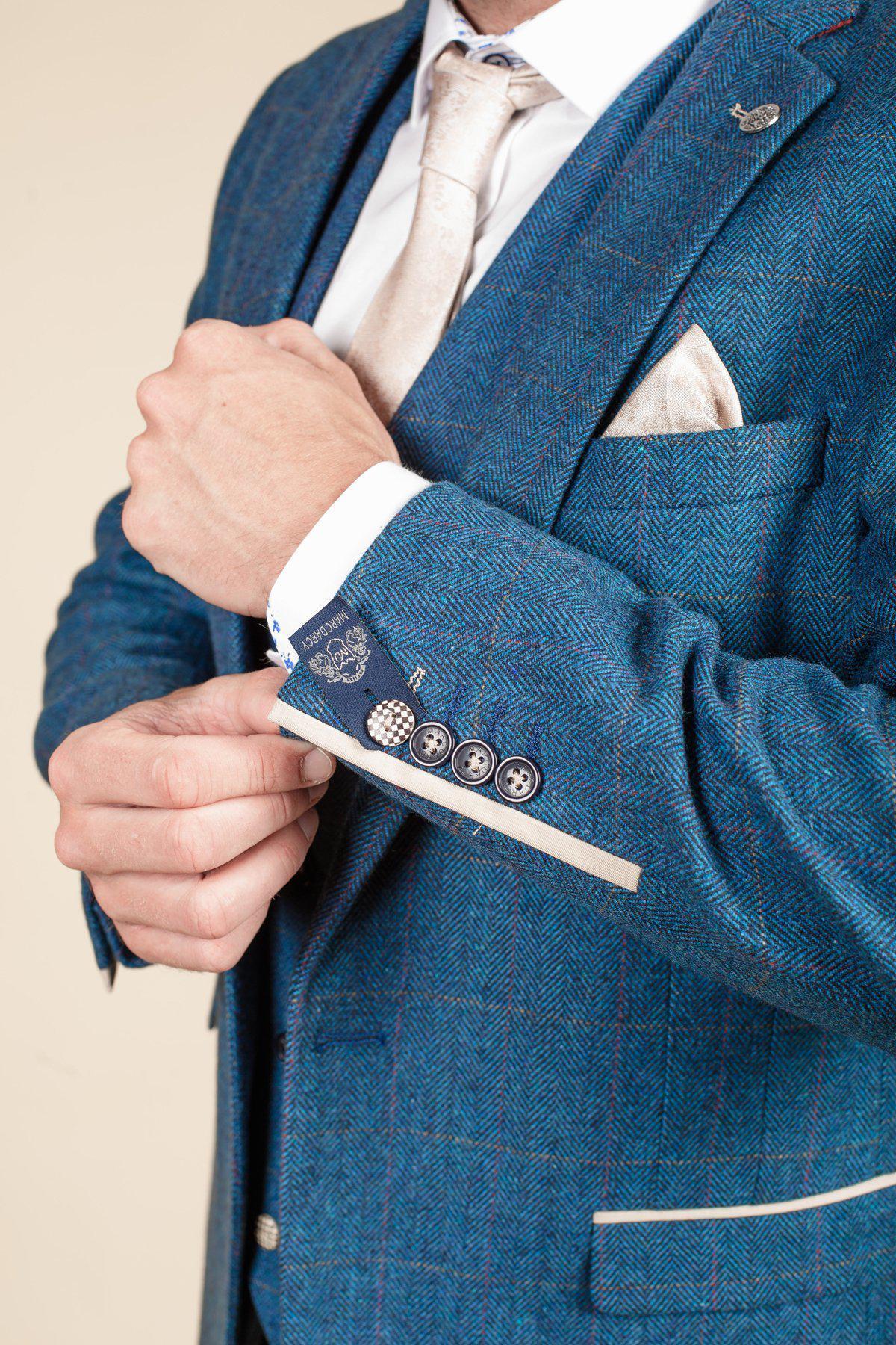 A man in the marcdarcy DION Blue Tweed Check Suit with Kelvin Cream Waistcoat adjusts his cuff, highlighting its smart buttons and silk pocket square—perfect for grooms seeking timeless wedding style.