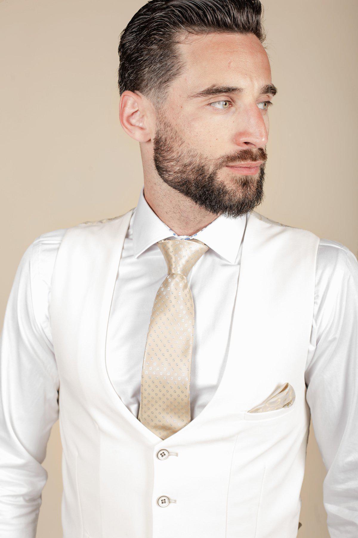 A man with short dark hair and a beard is wearing a marcdarcy DION blue tweed check suit and Kelvin cream waistcoat, paired with a light gold patterned tie and matching pocket square. He looks slightly to the right against a beige background.