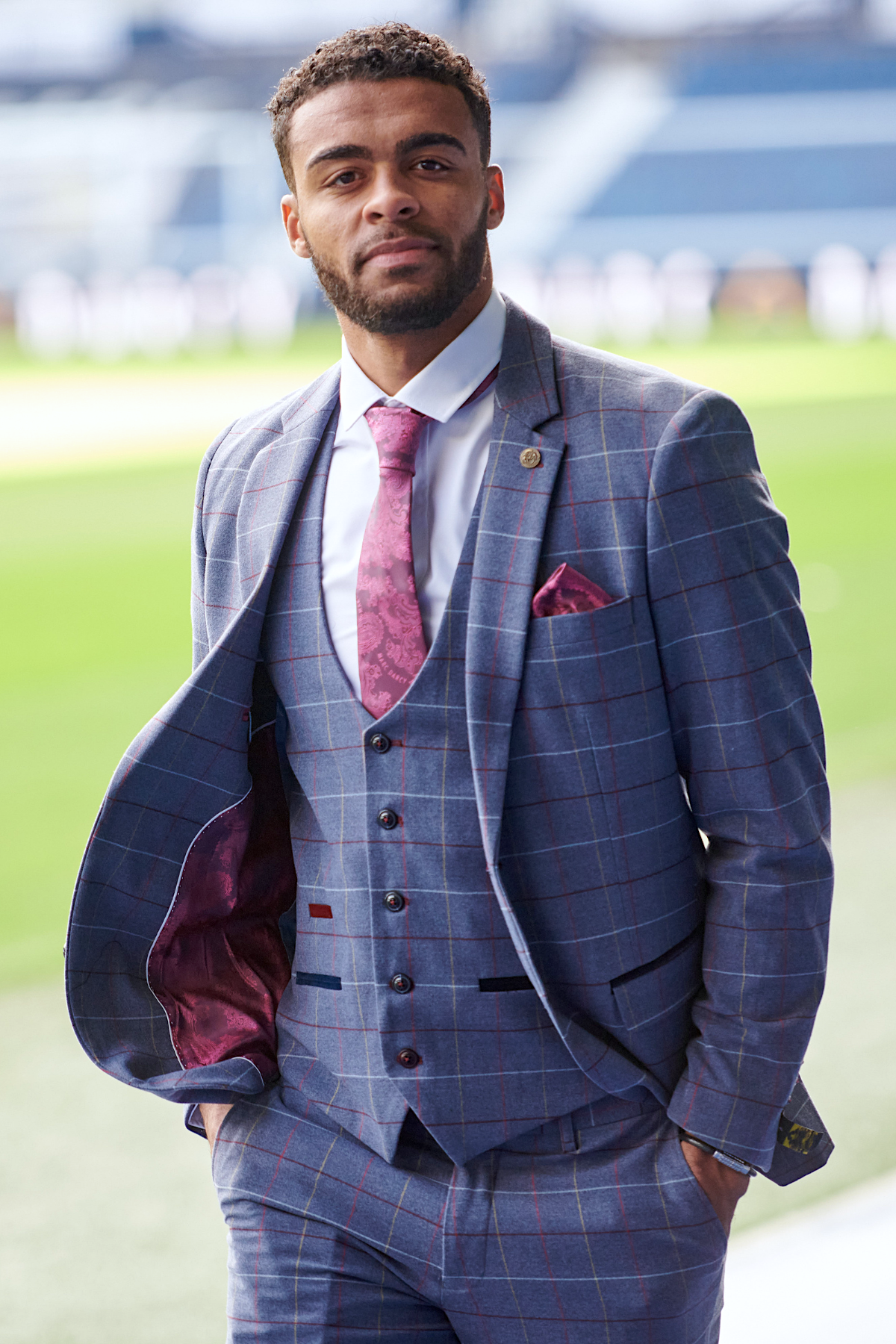 A man in the marcdarcy WBA Collection - Drake Sky Suit, as worn by Darnell Furlong, with a pink tie and pocket square stands confidently with hands in pockets, perfectly embodying formal style.