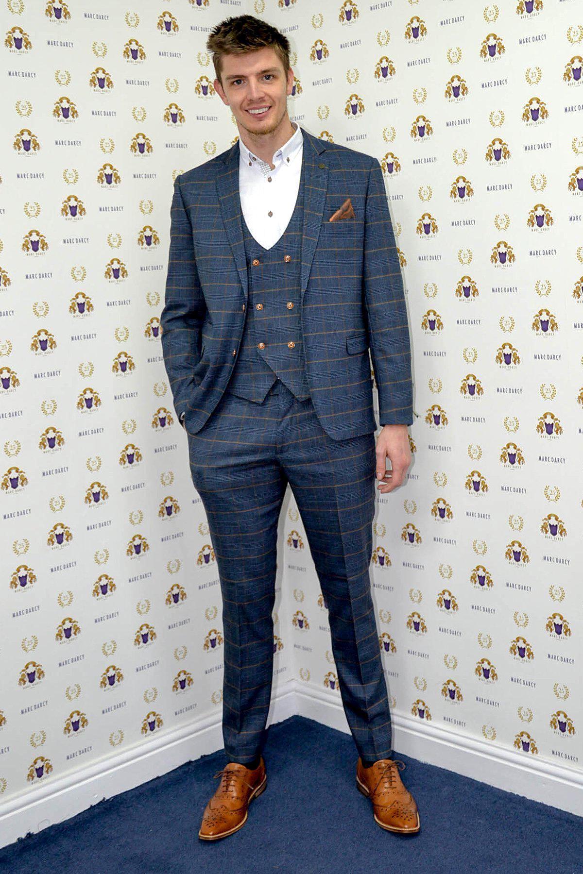 Newcastle United and England goalkeeper Nick Pope smiles in front of a wall with gold emblems and MARC DARCY text, wearing a marcdarcy Jenson Marine Check Suit.