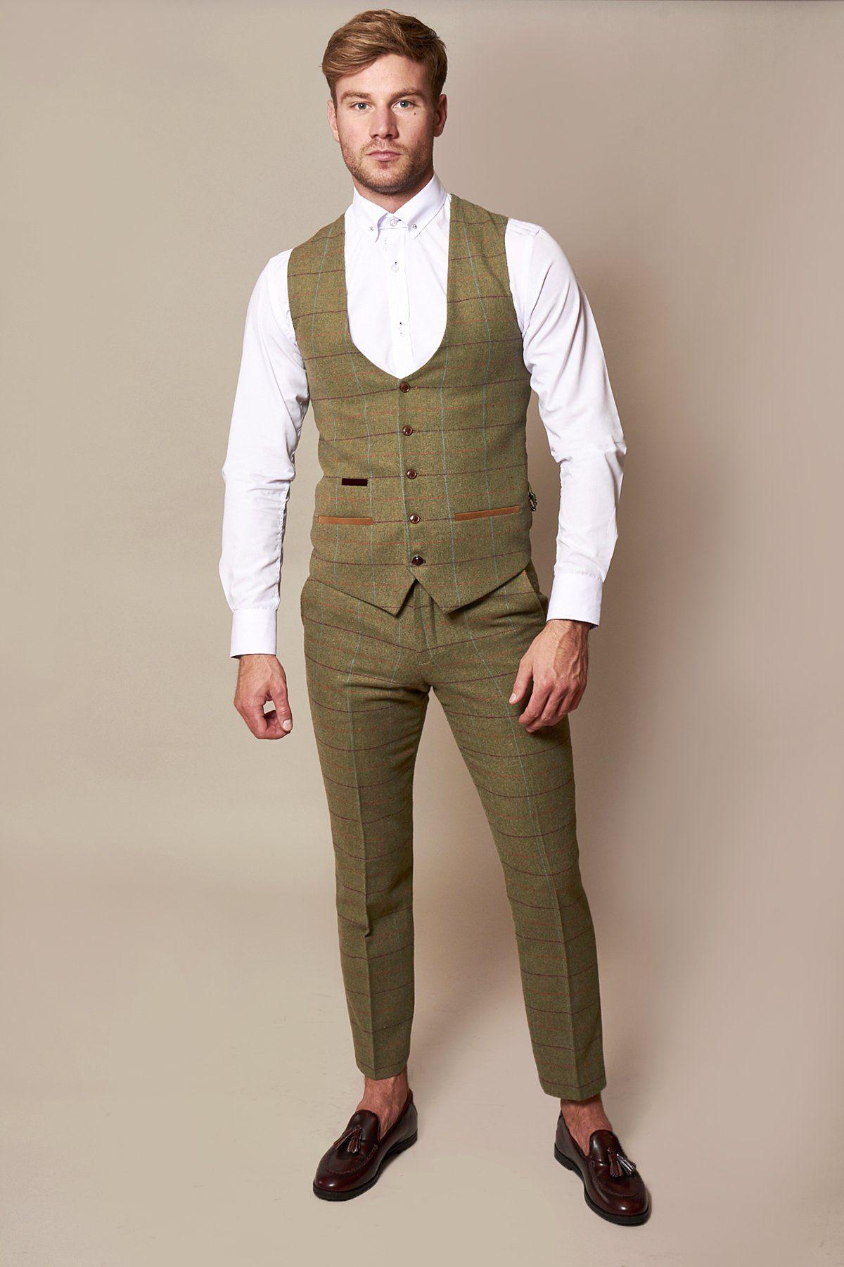 A man stands against a plain beige background wearing the marcdarcy ELLIS Moss Green Check Tweed Waistcoat over a white dress shirt, paired with a green plaid suit and brown dress shoes. He looks directly at the camera with a neutral expression.