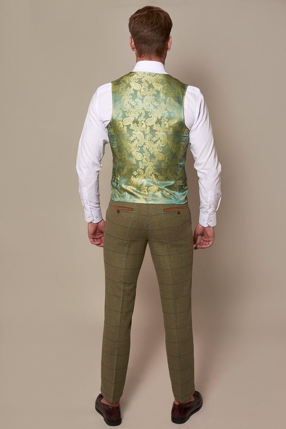 A man stands facing away in a slim fit white shirt, marcdarcy ELLIS Moss Green Check Tweed Waistcoat, green checked trousers, and brown dress shoes—a nod to Peaky Blinders style against a plain background.