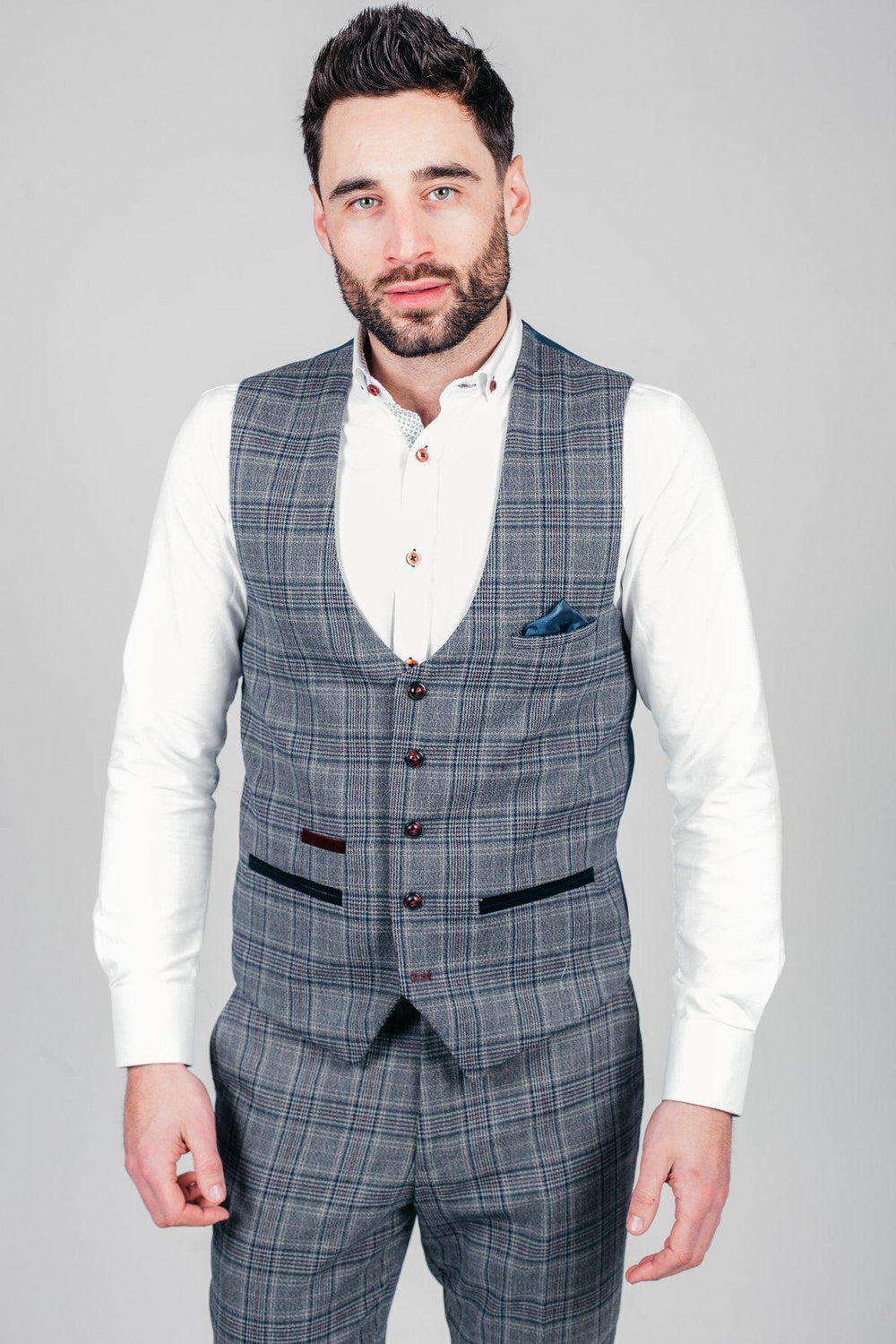 A man with short dark hair and a beard wears a white dress shirt and the marcdarcy ENZO - Blue Grey Check Tweed Single Breasted Waistcoat with matching pants, standing against a light grey background for a Peaky Blinders inspired look.