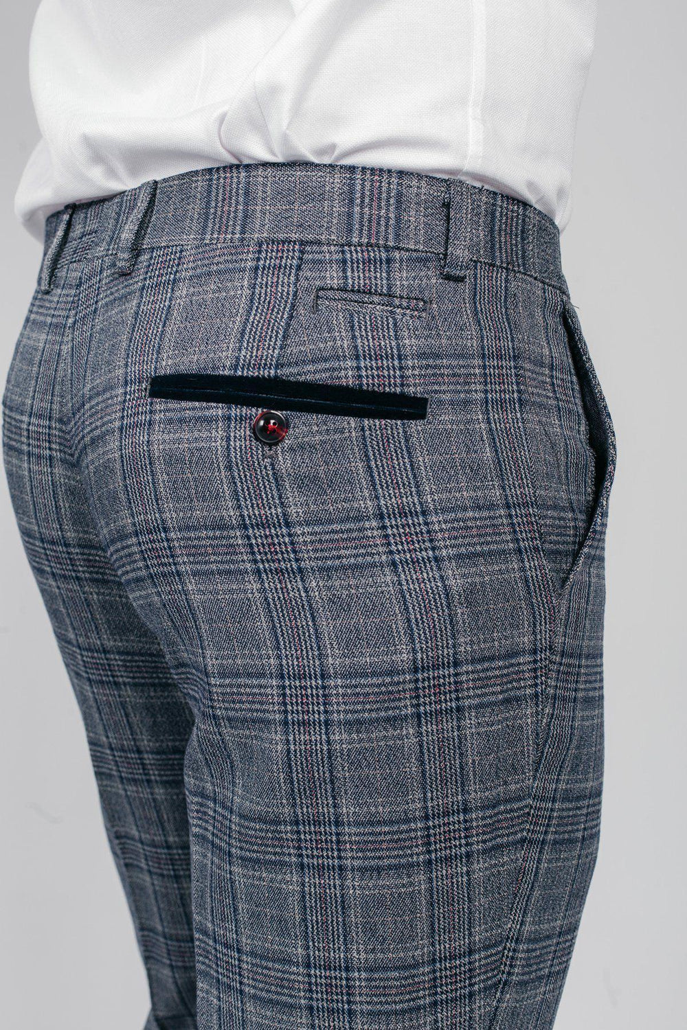 Close-up of a man wearing marcdarcy ENZO blue grey check tweed trousers with a white shirt. The trousers feature a navy velvet trim pocket and burgundy button, adding a subtle Peaky Blinders inspired detail.