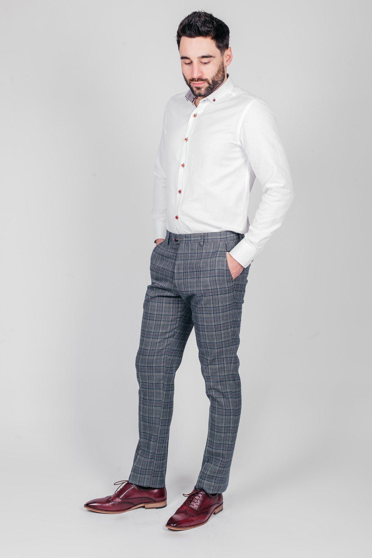 A man stands against a plain light background wearing a white button-up shirt, marcdarcy ENZO Blue Grey Check Tweed Trousers, and burgundy dress shoes, with his hands in his pockets and looking down.