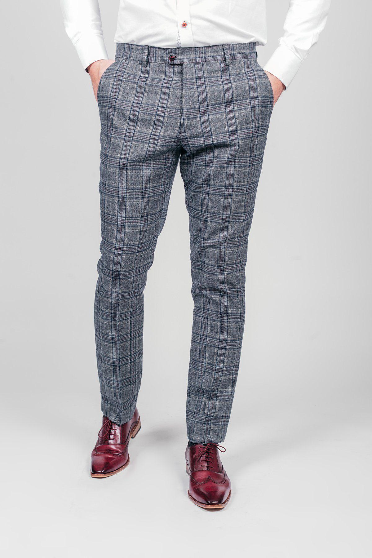 A person wearing marcdarcy ENZO Blue Grey Check Tweed Trousers, a white dress shirt, and burgundy dress shoes stands with hands in pockets against a plain light background.