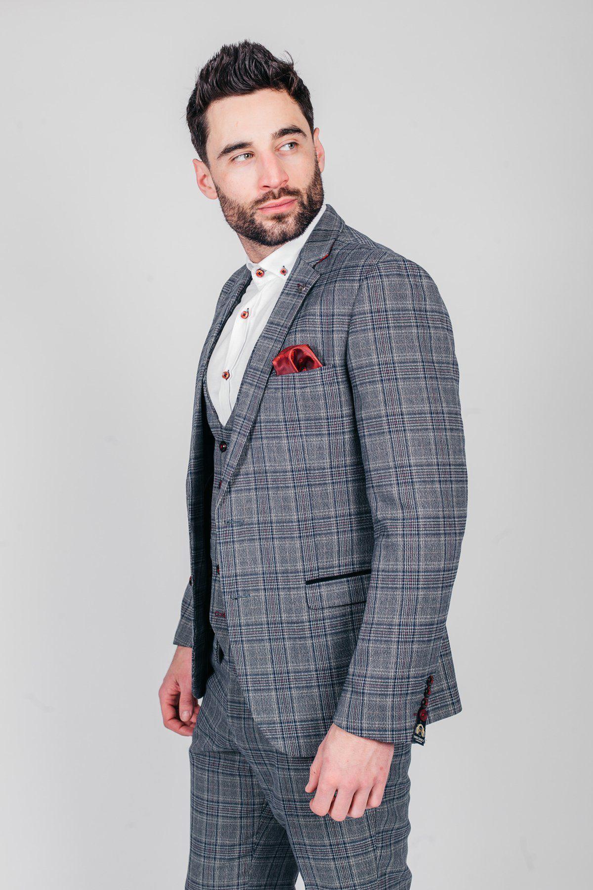 A man with dark hair and a beard models the marcdarcy ENZO Blue Grey Tweed Check Blazer with a white shirt and red pocket square, gazing right against a plain light background in a Peaky Blinders-inspired look.