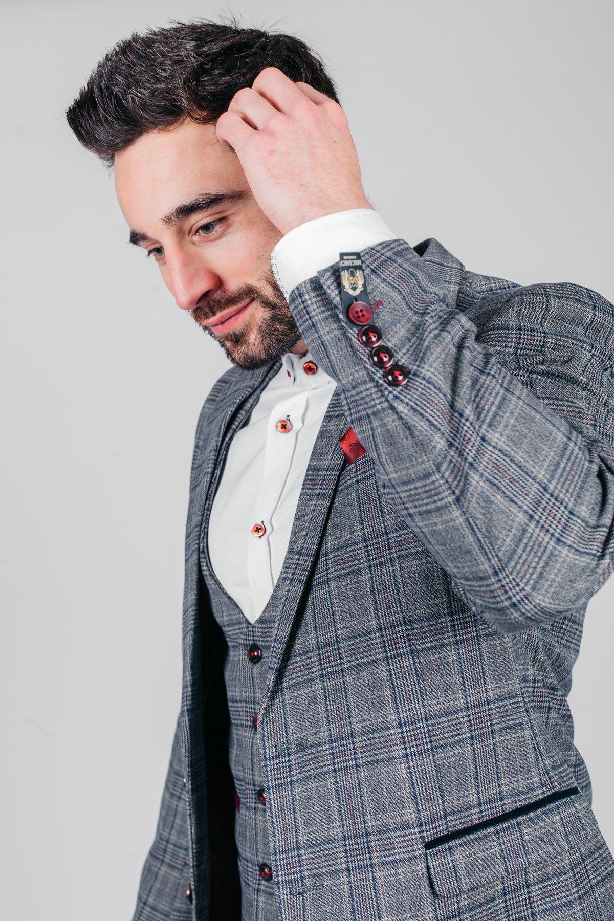 A man wearing the marcdarcy ENZO - Blue Grey Tweed Check Blazer with a white shirt touches his hair while looking down and smiling slightly, set against a plain light gray background.