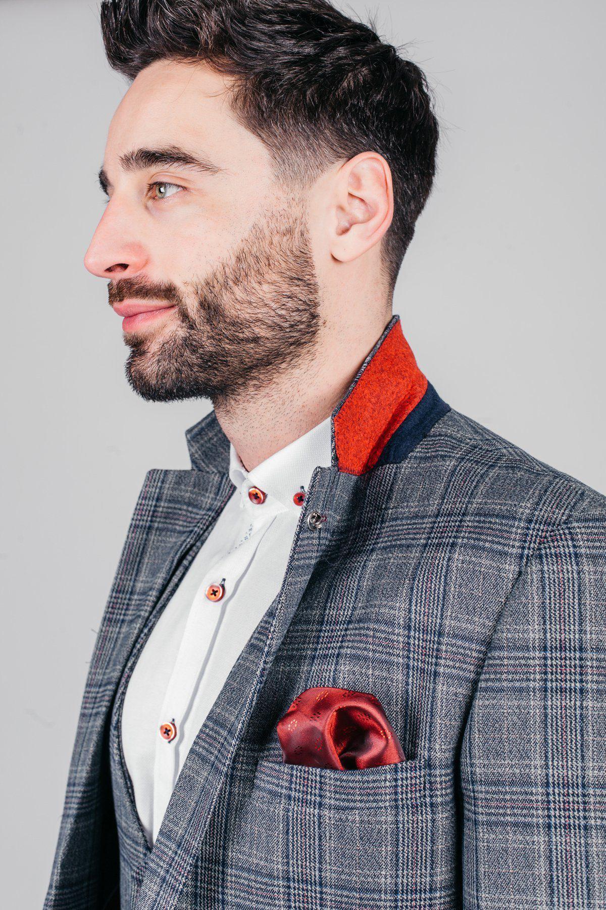 A man with dark hair and a beard wears the marcdarcy ENZO blue grey tweed check blazer, featuring a red and navy collar detail, white shirt with red buttons, and a red pocket square, posing against a light grey background.