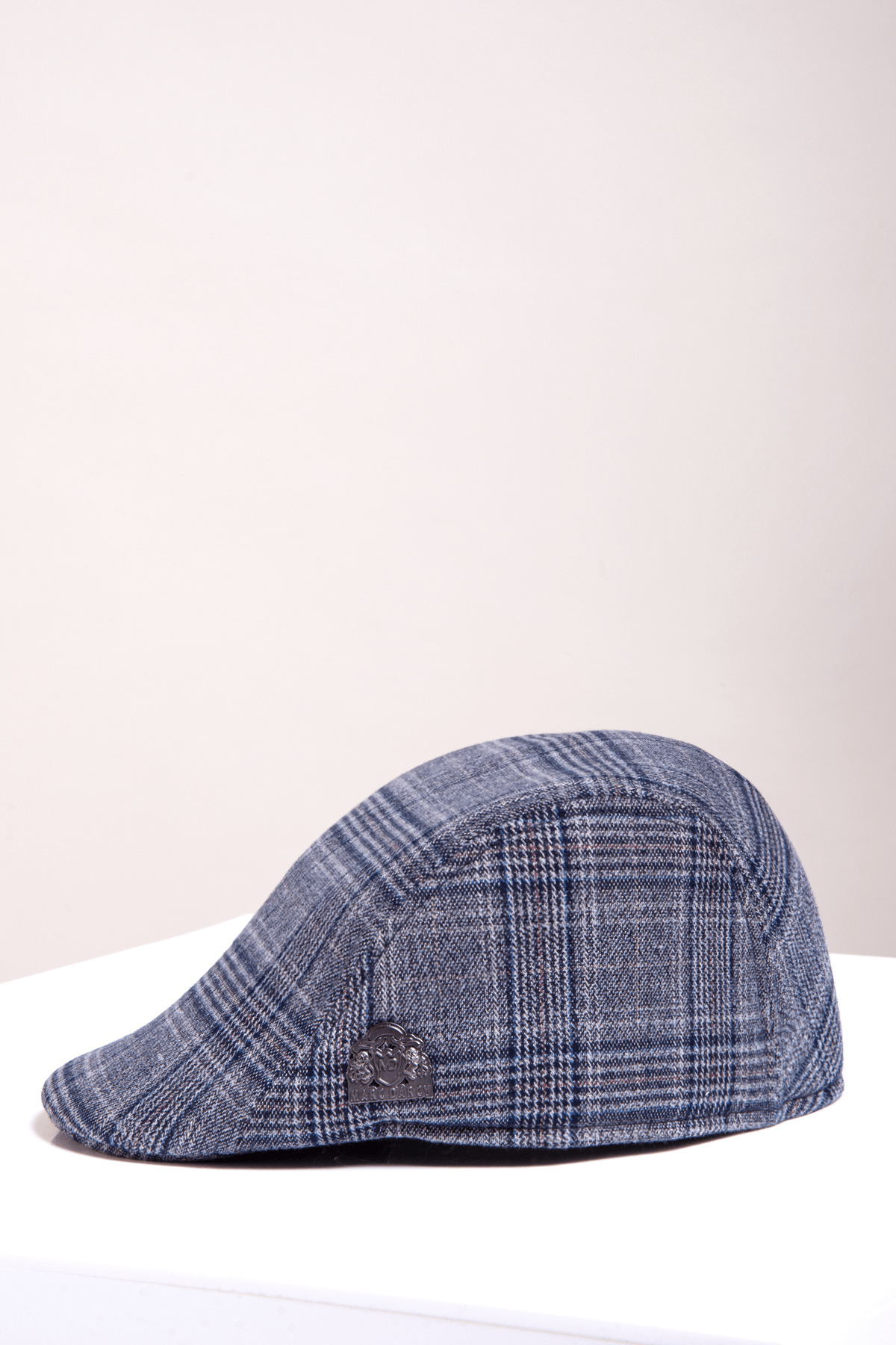 The ENZO - Blue Grey Tweed Flat Cap by Accessory features a blue and gray Prince of Wales check and a small Marc Darcy badge on the side, shown on a white surface with a plain light background.