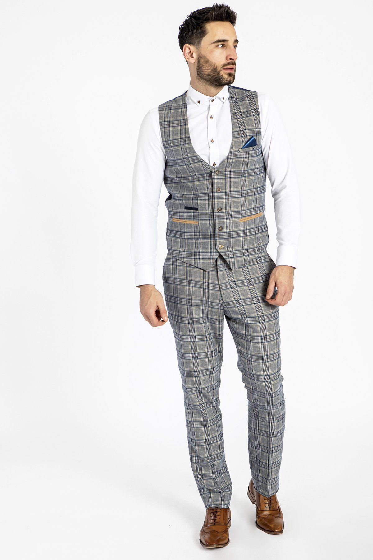 A man in a gray Prince of Wales check three-piece suit with a marcdarcy ENZO - Sky Stone Check Tweed Single Breasted Waistcoat, white shirt, and brown dress shoes stands against a white background, looking slightly left.