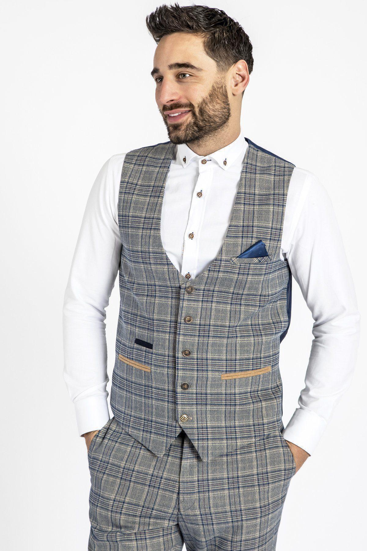 A man wears the marcdarcy ENZO - Sky Stone Check Tweed Single Breasted Waistcoat with matching trousers and a white shirt, hands in pockets and smiling, against a plain white background.