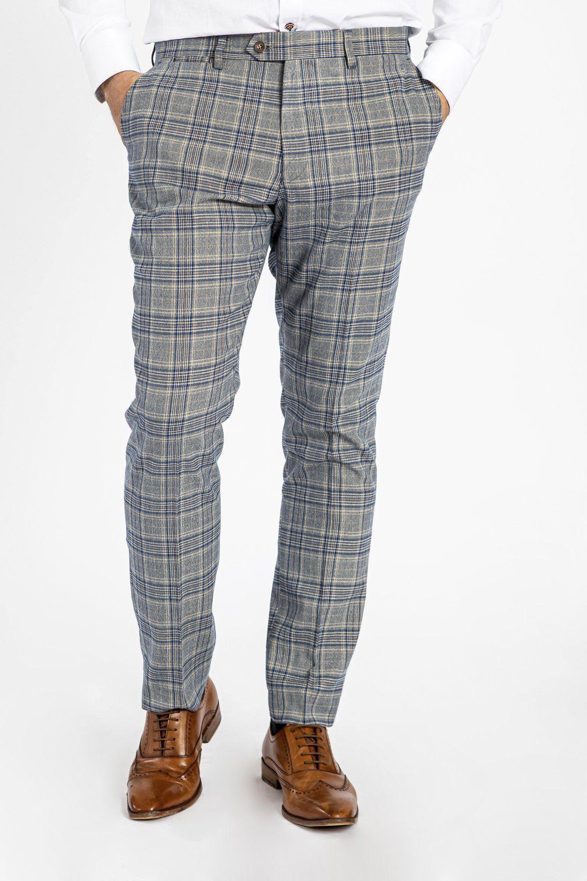 A man wearing marcdarcy ENZO Sky Stone Check Tweed Trousers and brown wingtip shoes stands with his hands in his pockets against a white background.