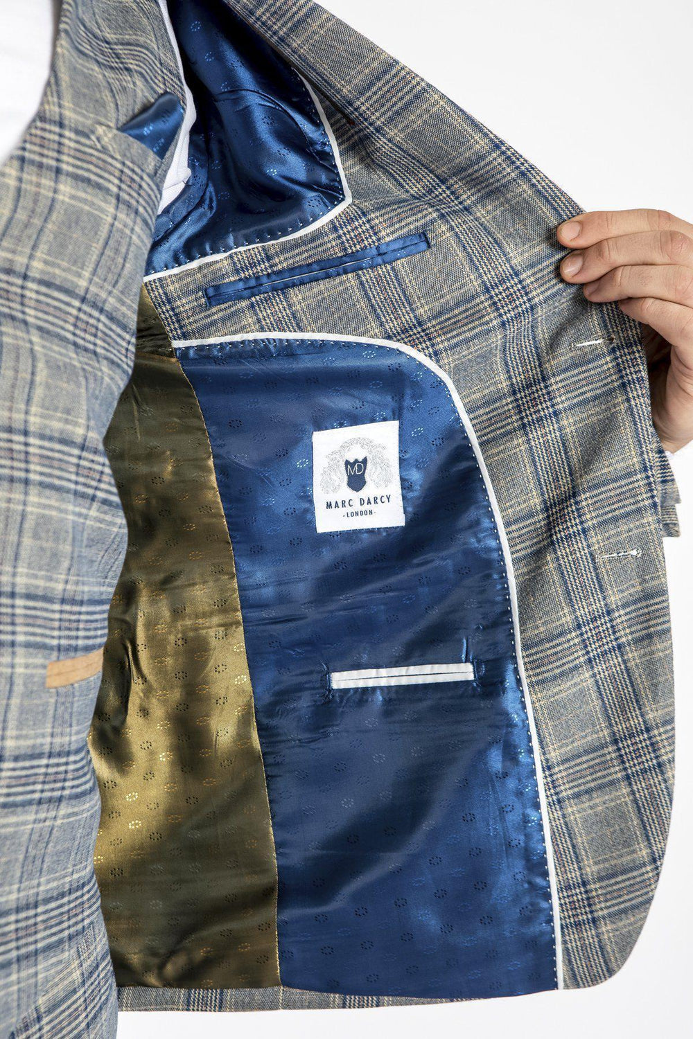 A person holds open a marcdarcy ENZO - Sky Stone Tweed Check Blazer to show its blue and gold inner lining with the marcdarcy label, revealing their hand and part of a white shirt.