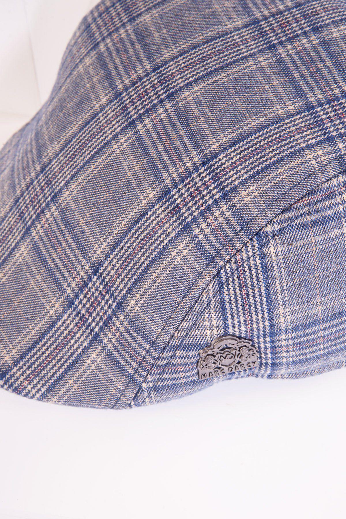 A close-up of the ENZO - Sky Stone Tweed Flat Cap by Accessory, featuring blue and gray Prince of Wales check and a metallic Harris Tweed emblem on the side, resting on a white surface.