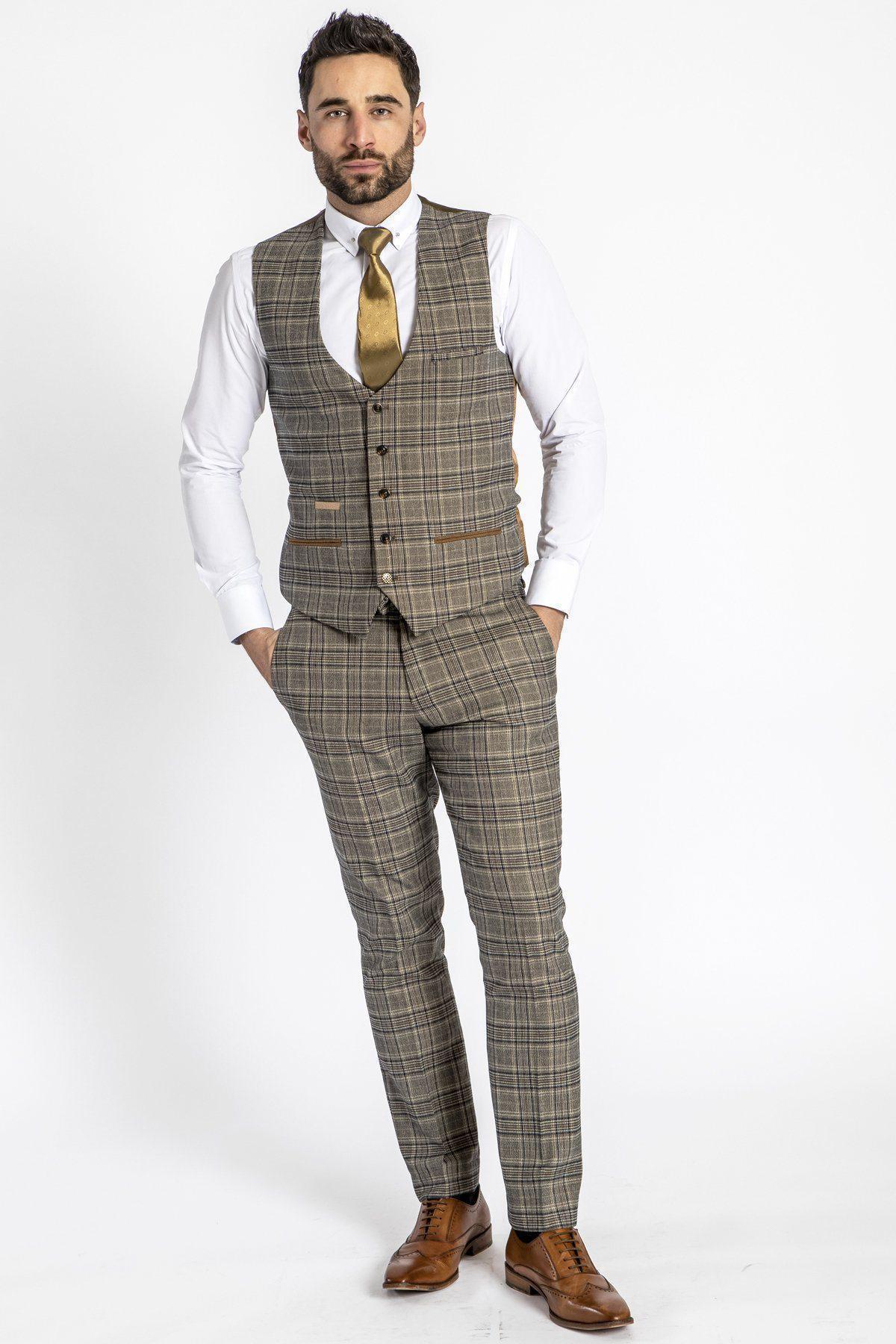 A man stands against a white background wearing a marcdarcy ENZO Tan Check Tweed Single Breasted Waistcoat, part of a Peaky Blinders-inspired plaid three-piece suit, with brown shoes, white shirt, gold tie; hands in pockets, neutral expression.