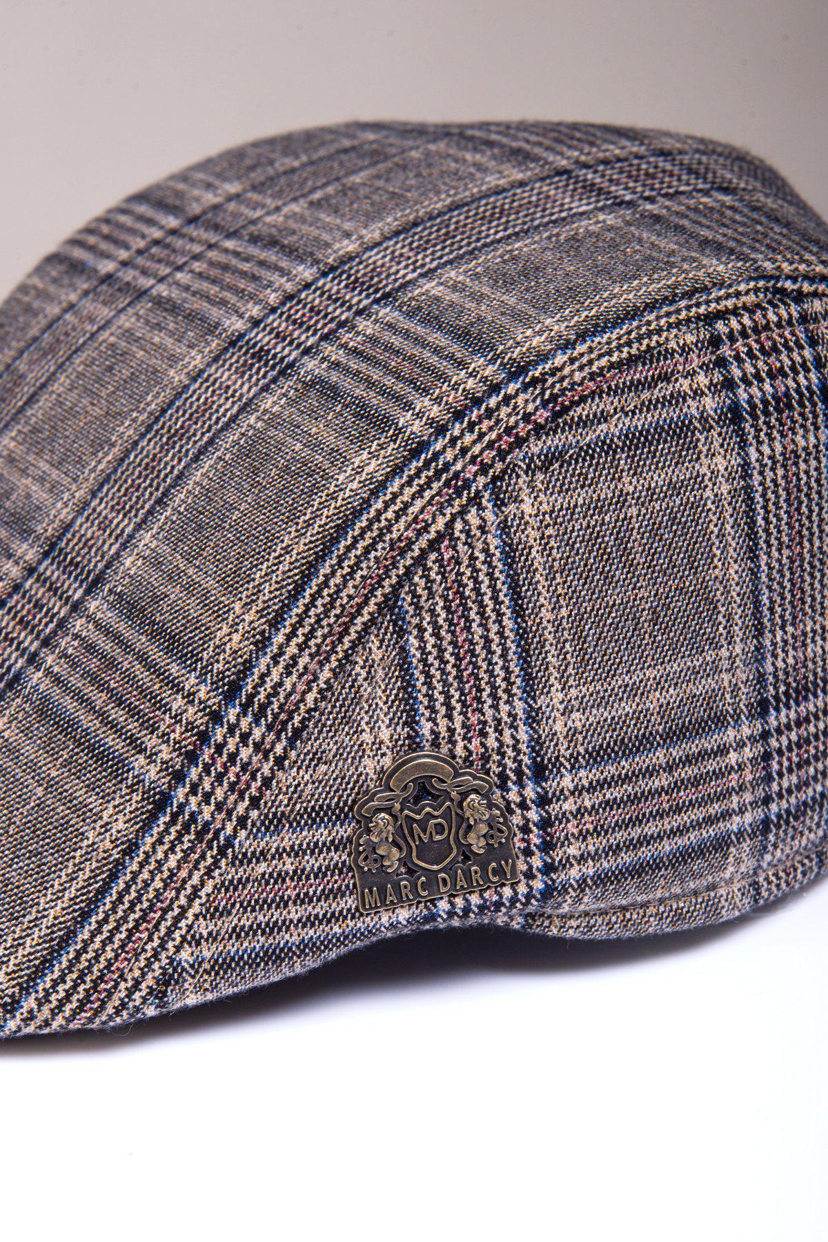 A close-up of the ENZO - Tan Tweed Flat Cap by Accessory, showcasing its Prince of Wales check pattern in brown and grey plaid with a metallic logo pin on the side.