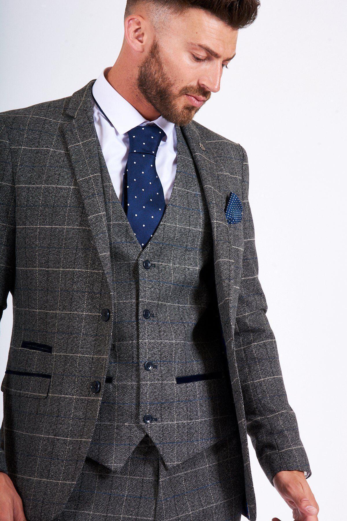 Former Arsenal Midfielder and Invincible Gilberto Silva wears a marcdarcy Scott Grey Tweed Check Blazer & Waistcoat, styled with a white shirt and blue polka-dot tie, looking downwards against a plain background.