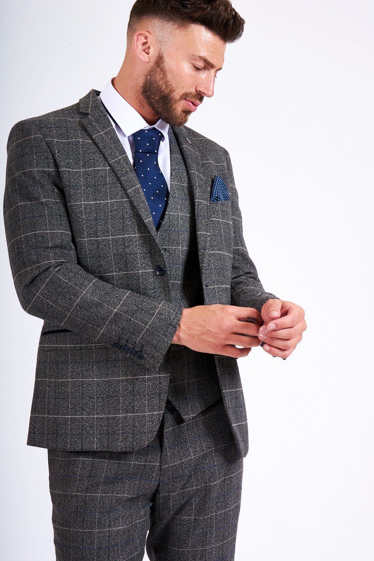 Former Arsenal Midfielder Gilberto Silva wears a marcdarcy Scott Grey Tweed Check Blazer & Waistcoat, paired with a white shirt, navy polka dot tie, and patterned pocket square as he adjusts his cuff and looks down.