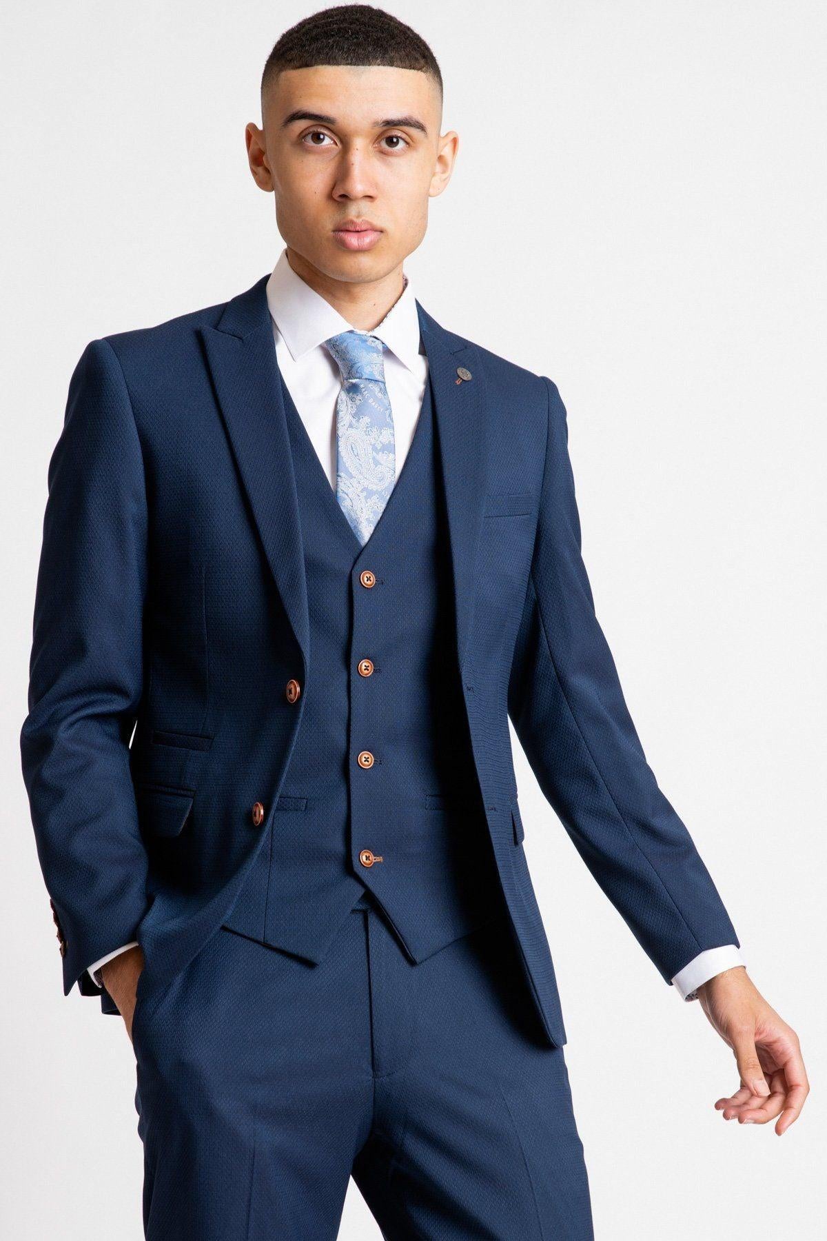 Im A Celebrity Get Me Out Of Here 2022 runner-up Owen Warner wears a marcdarcy Max royal blue suit with a slim fit blazer, light blue patterned tie, and white dress shirt, posing with one hand in his pocket against a plain white background.