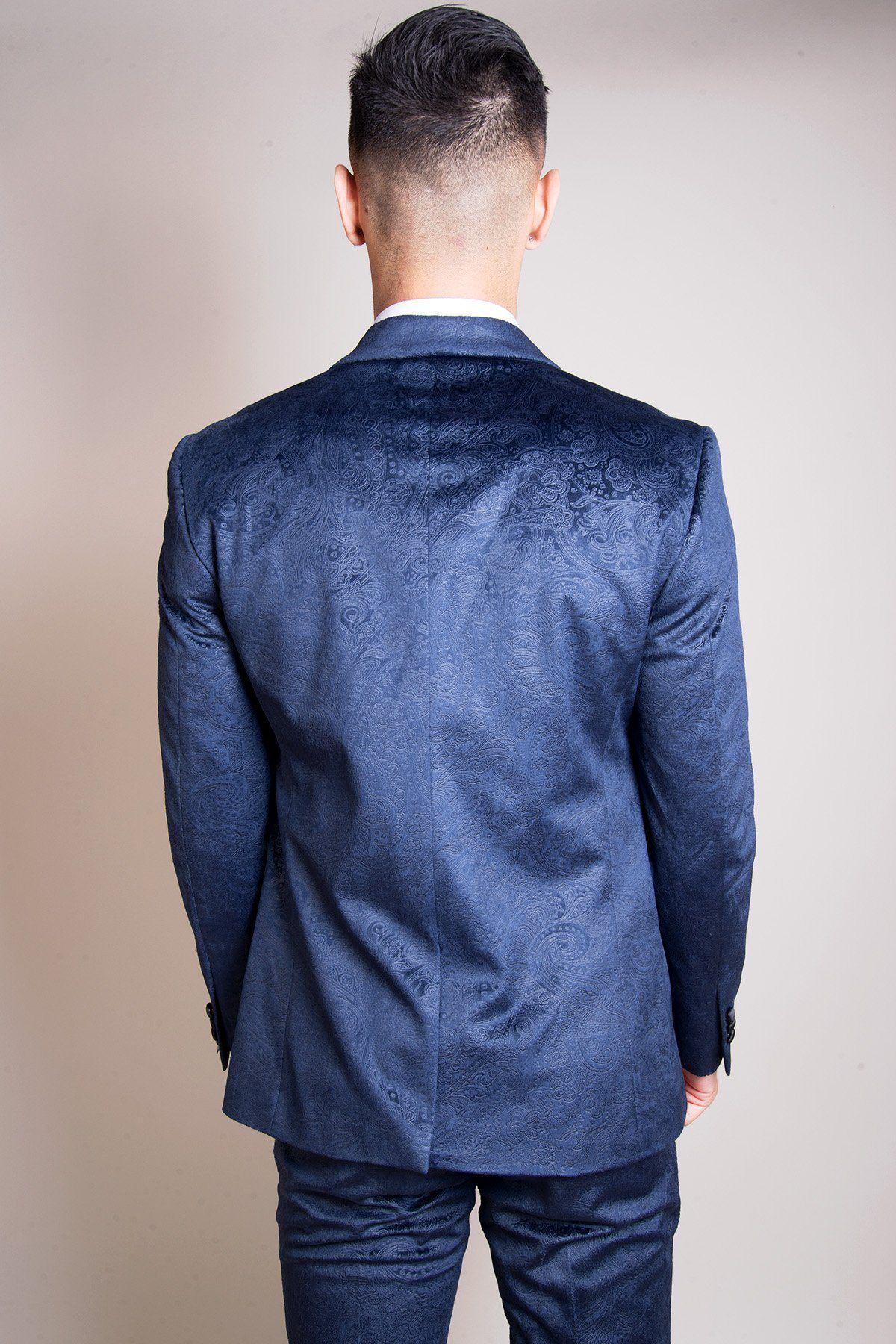 Will Mellor, as Harvey Gaskell in Coronation Street, wears the Marc Darcy Simon Velvet Blazer & Waistcoat, featuring dark blue patterned velvet with satin lapels and a white shirt, standing against a plain light background.