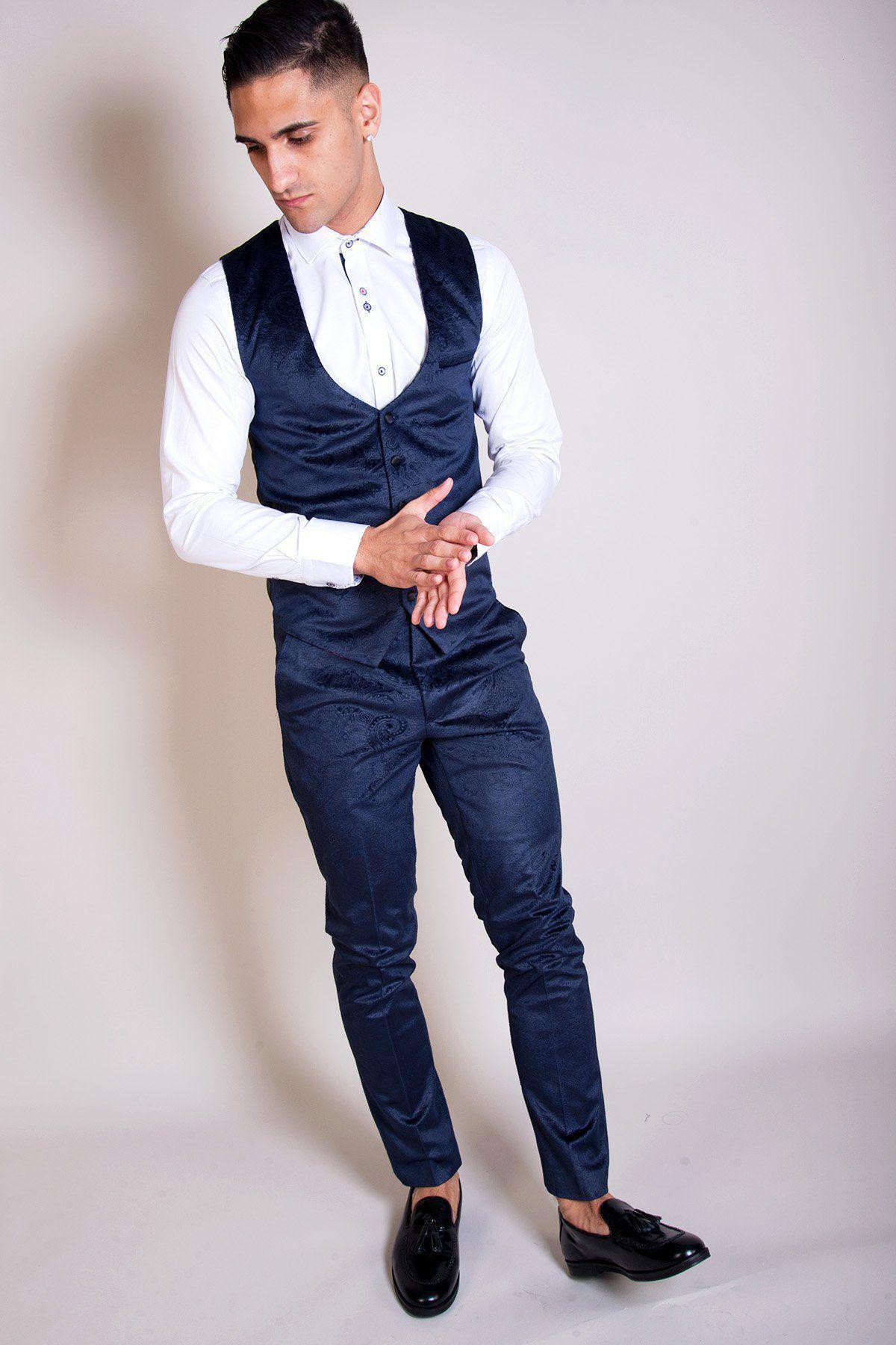 Will Mellor as Harvey Gaskell on Coronation Street wears the Simon Velvet Blazer & Waistcoat by Marc Darcy—dark blue velvet vest, white shirt, and matching pants—standing with hands clasped, looking down.