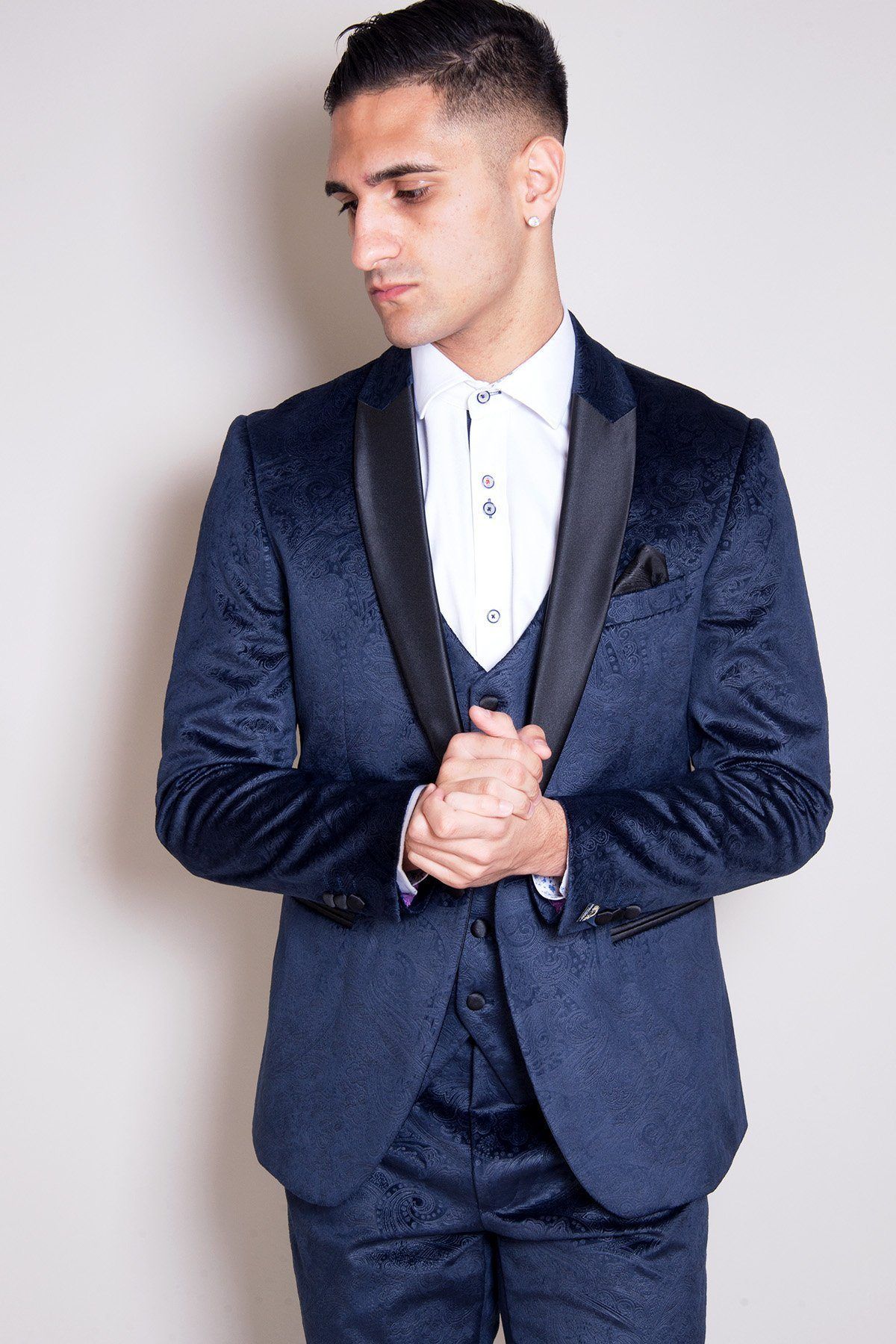 Coronation Streets Will Mellor (Harvey Gaskell) wears the Simon Velvet Blazer & Waistcoat by Marc Darcy—a slim-fit, dark blue patterned tux blazer with satin lapels and a white shirt, standing against a plain light background.