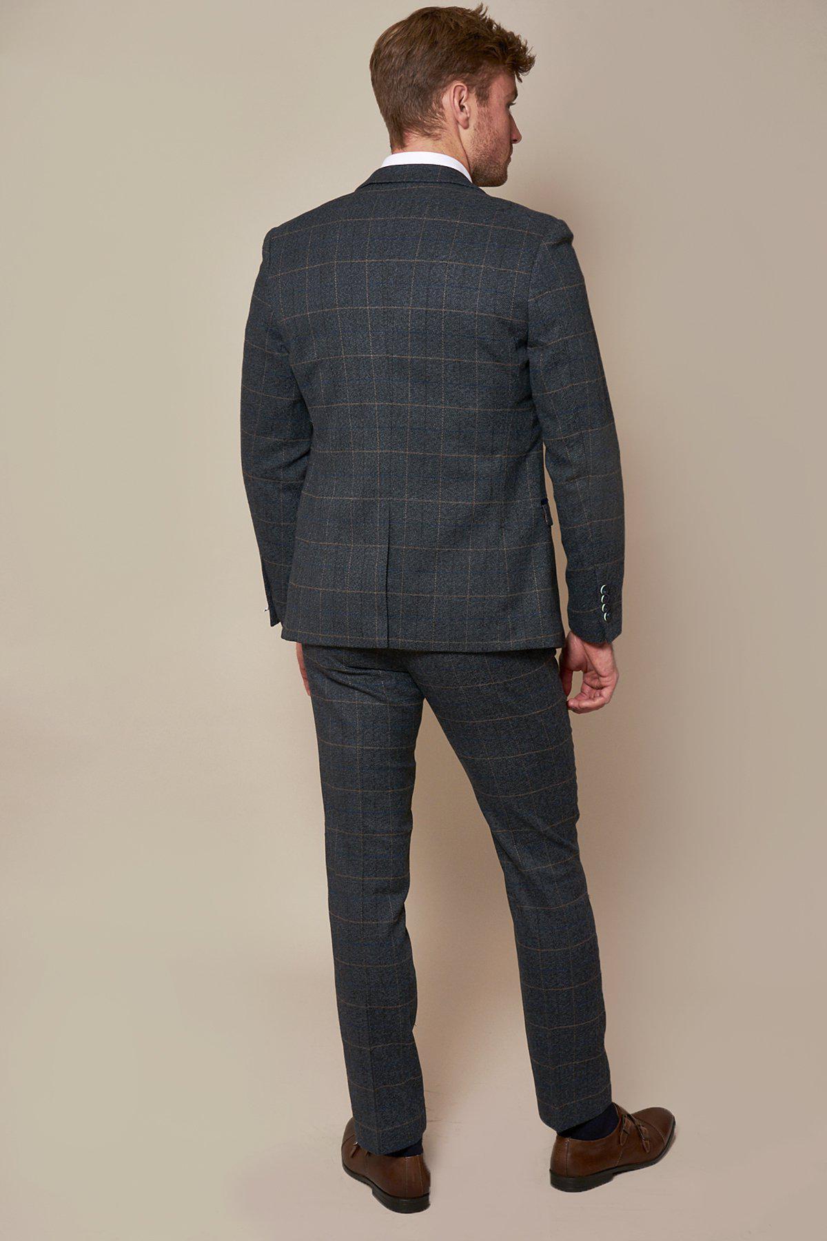Alex Beresford, wearing a marcdarcy Scott Blue Tweed Check Suit and white shirt, stands with his back to the camera against a plain beige background.