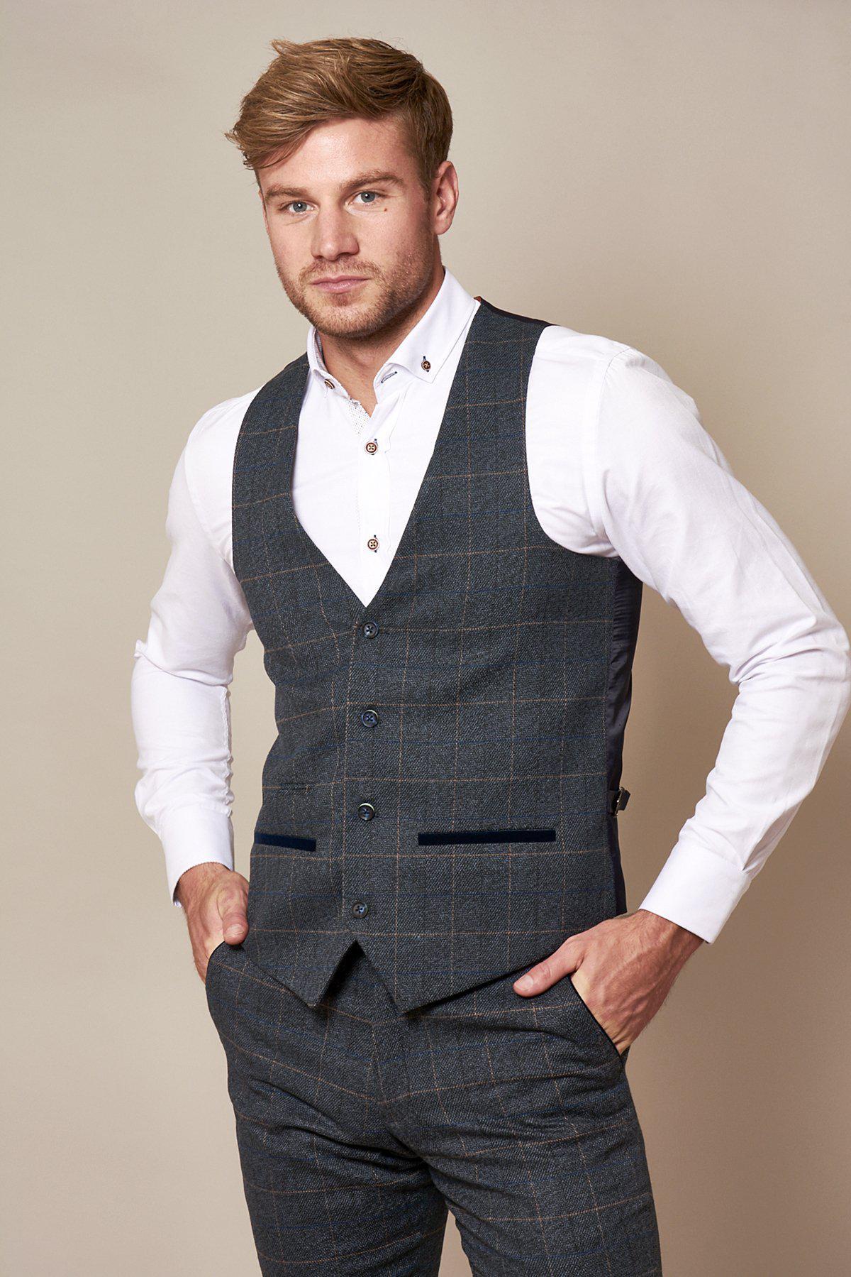 Alex Beresford wears the marcdarcy Scott Blue Tweed Check Suit, featuring a classic check pattern. He stands facing the camera with hands in pockets, sporting short light brown hair and a neatly trimmed beard.