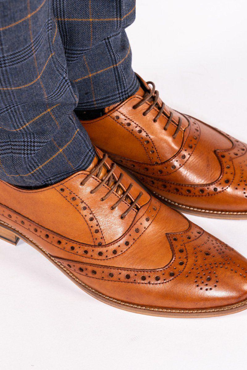 Close-up of a person wearing Marc Darcy’s GRAYSON tan leather wingtip brogue shoes with handcrafted details, paired with blue plaid trousers with orange lines, standing on a white background.