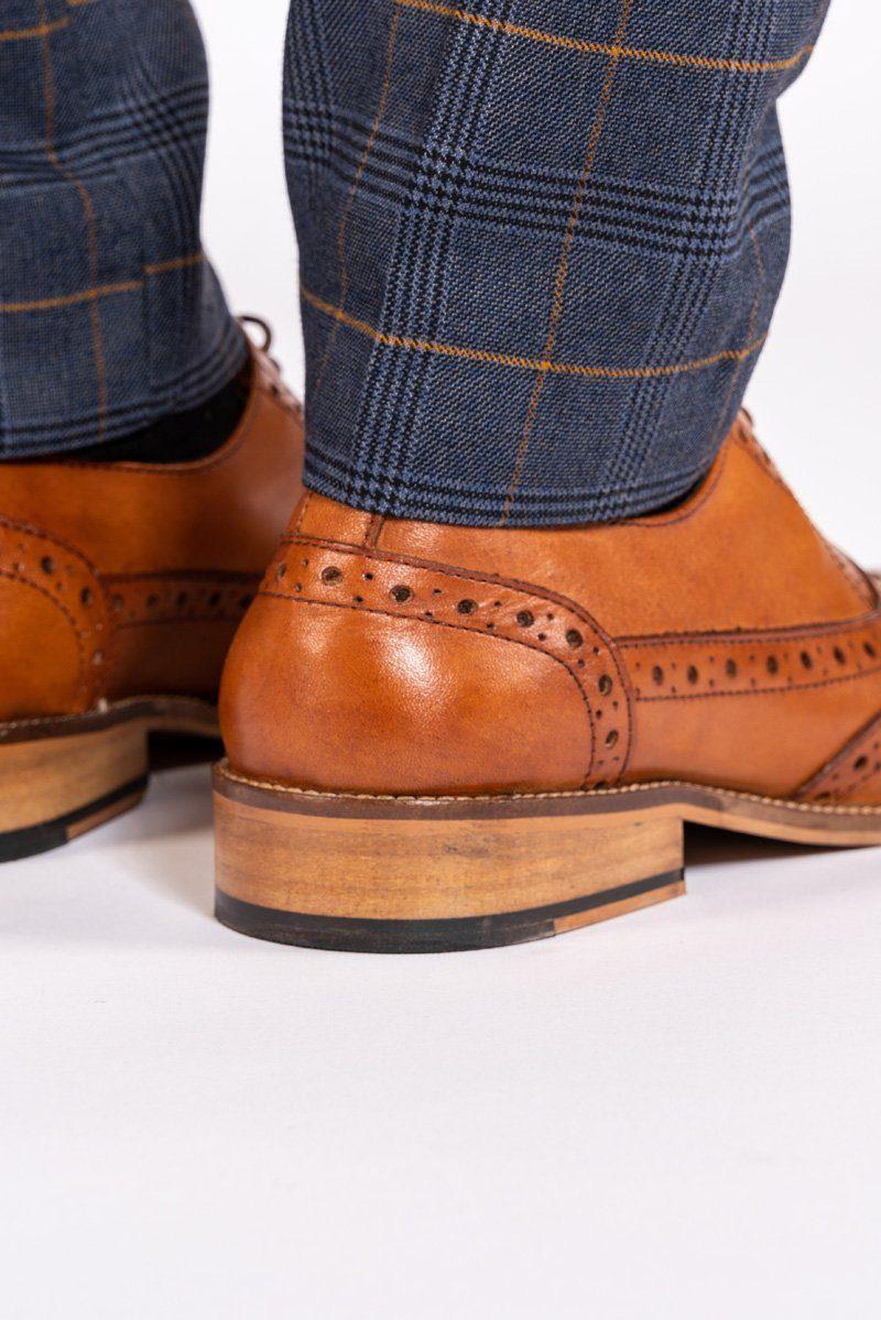Close-up of a man's legs wearing Marc Darcy’s GRAYSON Tan Leather Wingtip Brogue Shoes with blue plaid pants, set against a white background.