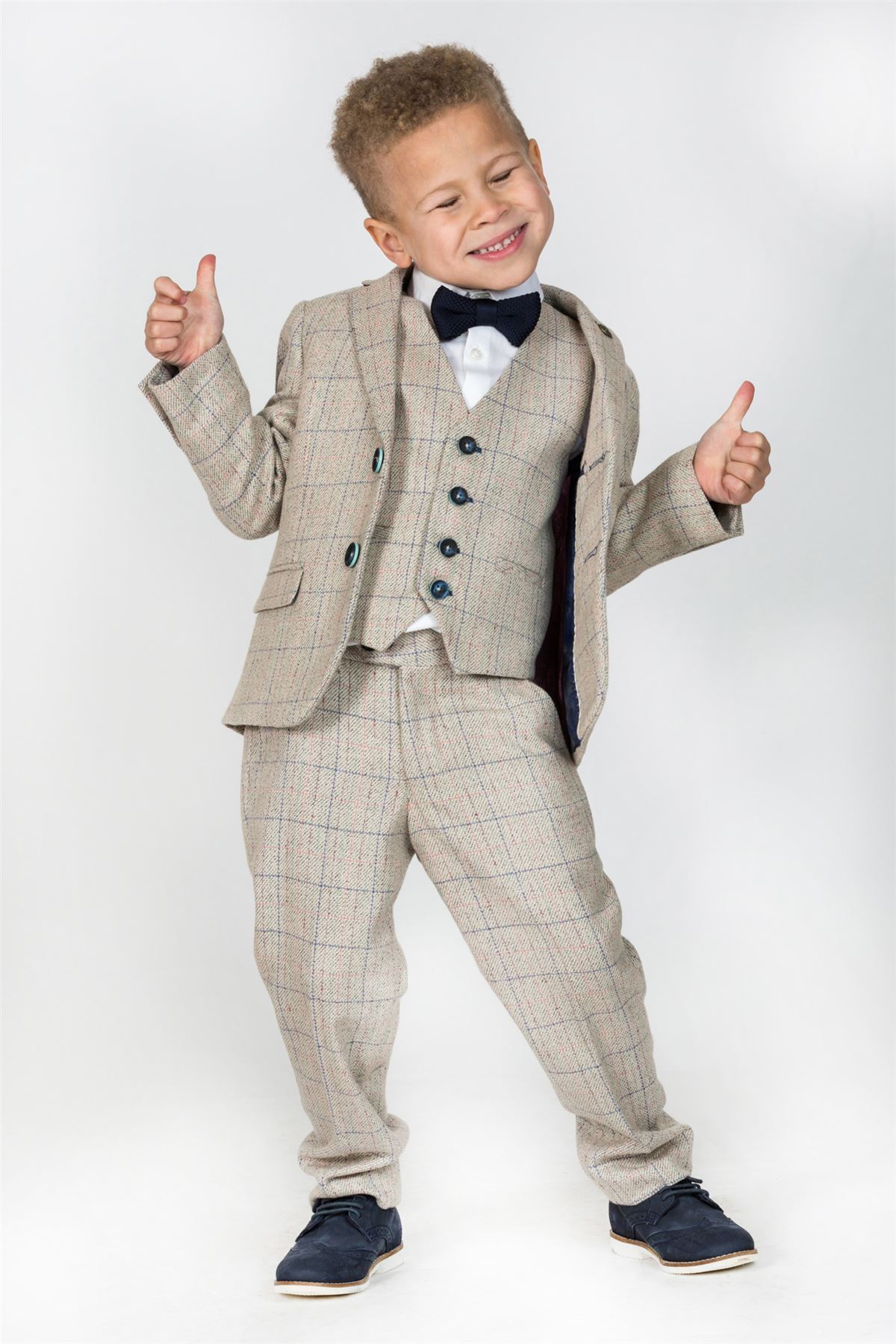 A young boy in a marcdarcy HARDING Children's Cream Tweed Check Three Piece Suit gives two thumbs up and smiles.