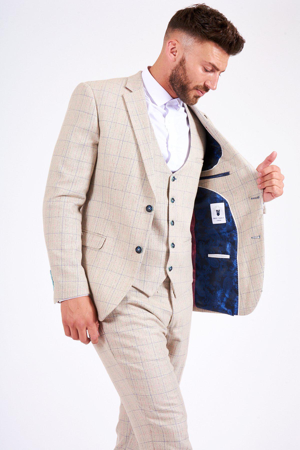 A man in the marcdarcy HARDING - Cream Tweed Check Print Blazer and a white shirt looks down while opening his jacket to reveal a dark blue patterned lining.