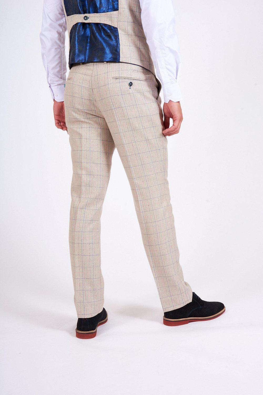 A man faces away, wearing marcdarcy HARDING cream tweed check print trousers, a matching vest with a blue satin back, a white shirt, and black shoes with red soles, set against a plain white background.