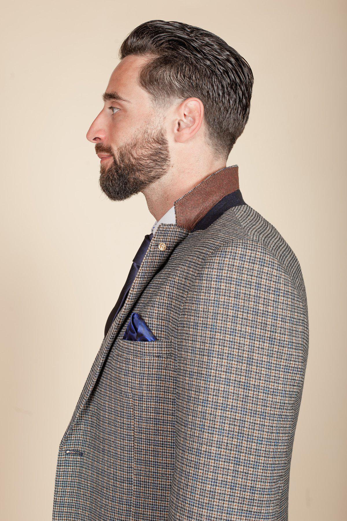 Man in profile view wearing a slim fit marcdarcy HARDWICK navy tan tweed check blazer with brown suede collar, navy tie, and blue pocket square. He has dark slicked-back hair and a trimmed beard.