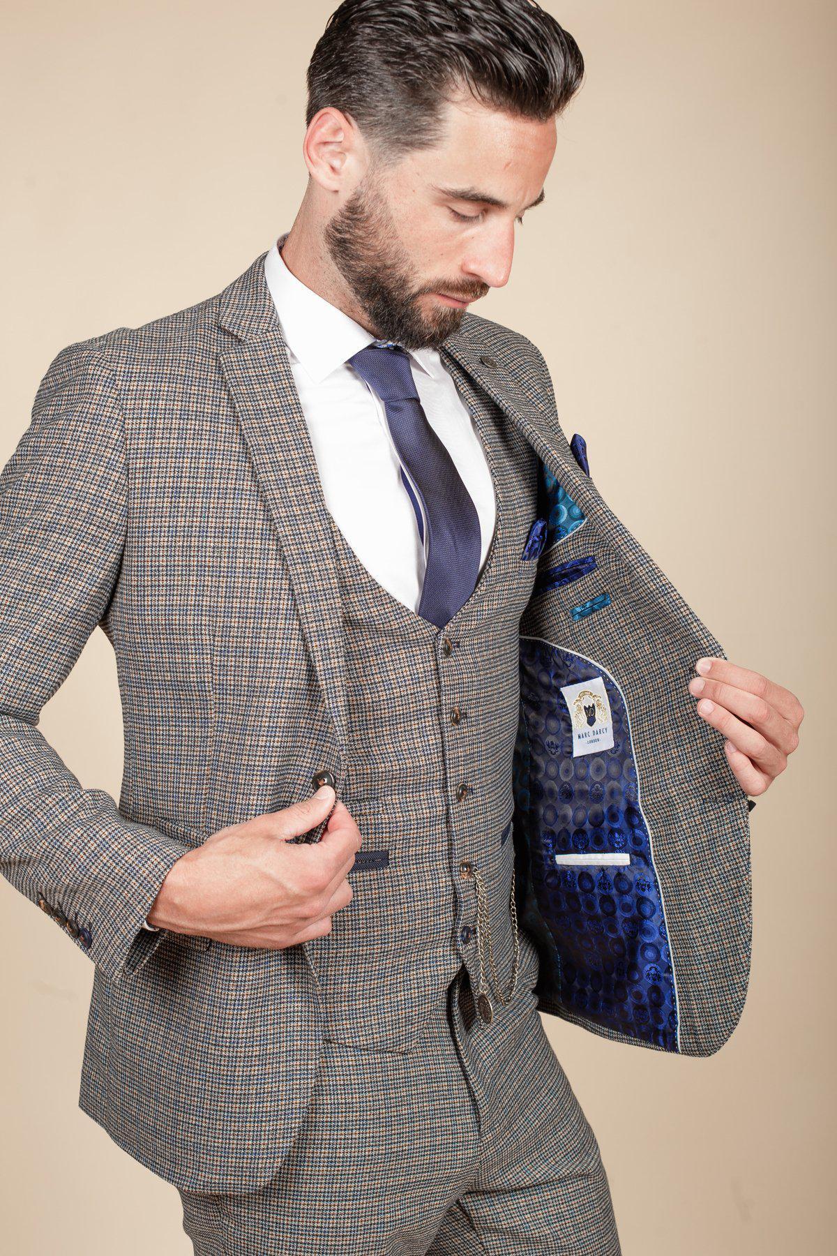 A man wearing the marcdarcy HARDWICK Navy Tan Tweed Check Blazer, paired with a white shirt and navy tie, looks down and opens his jacket to show its blue patterned lining and detailed inside pockets.