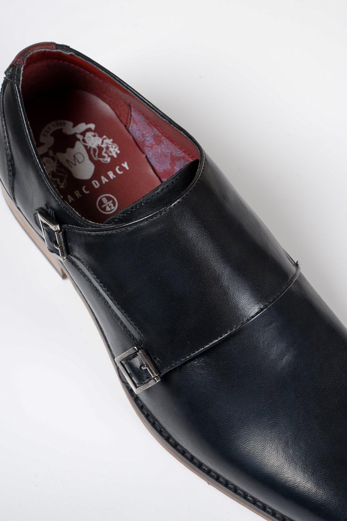 The Marc Darcy HARRIS is a black leather double strap monk shoe with silver buckles, crafted from full grain leather, featuring hand-stitched details, maroon lining, and the brand logo on the insole. Shown against a white background.