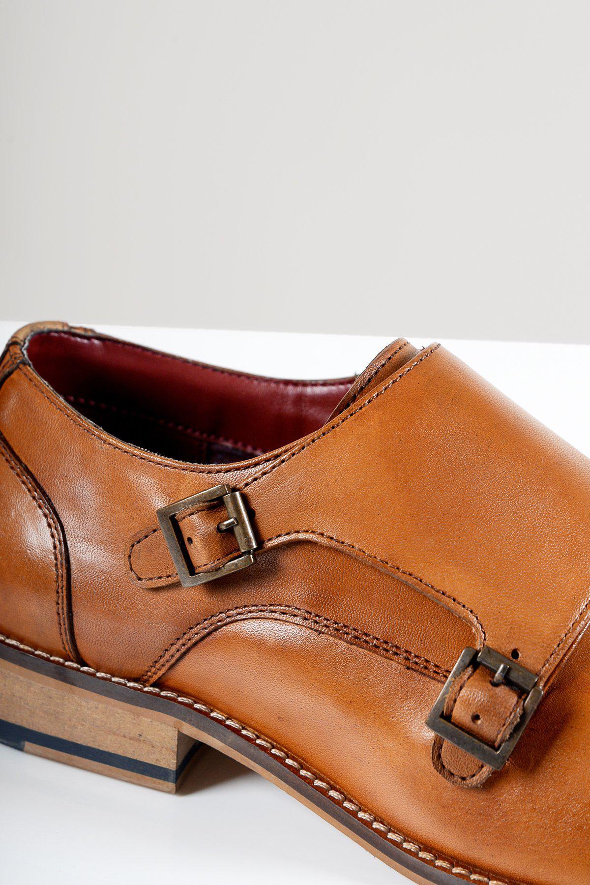 The HARRIS Tan Leather Double Strap Monk Shoe by Marc Darcy features full grain leather, antique brass buckles, contrast stitching, red lining, and a stacked wooden heel, shown here on a white surface.