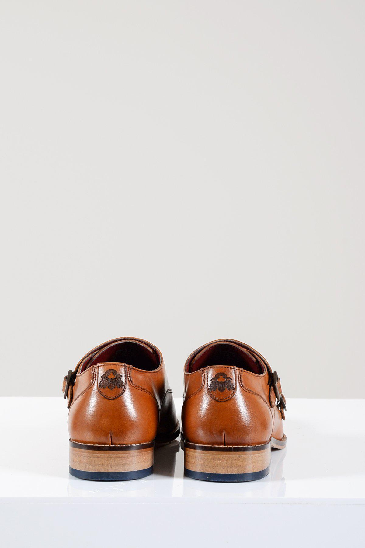 The HARRIS Tan Leather Double Strap Monk Shoe by Marc Darcy, crafted from brown vegetable-tanned leather with wooden heels and hand-stitched details, is shown from the back on a white surface with a light gray background.