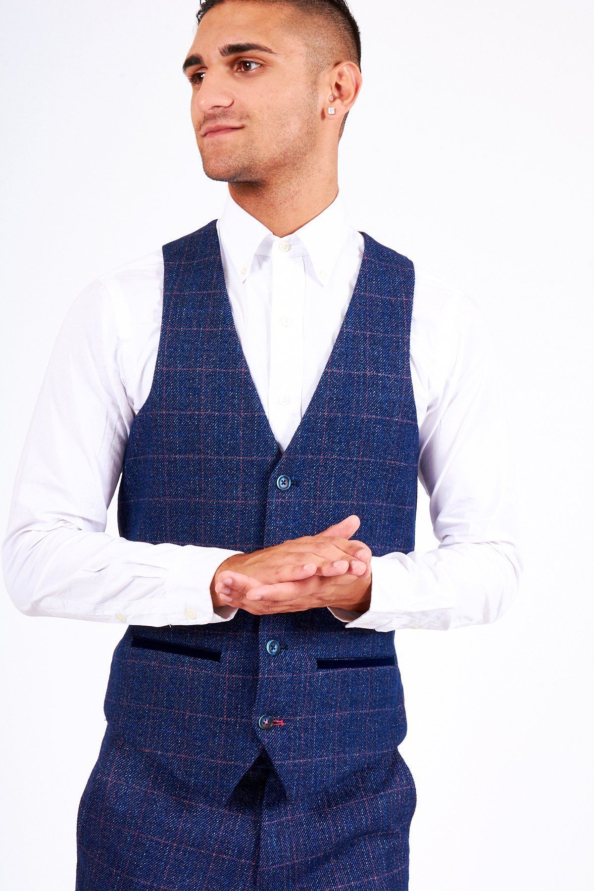 A man in wedding attire wears the marcdarcy HARRY Indigo Single Breasted Tweed Check Waistcoat over a white shirt and blue trousers, standing with hands loosely clasped and gazing to the side against a plain white background.