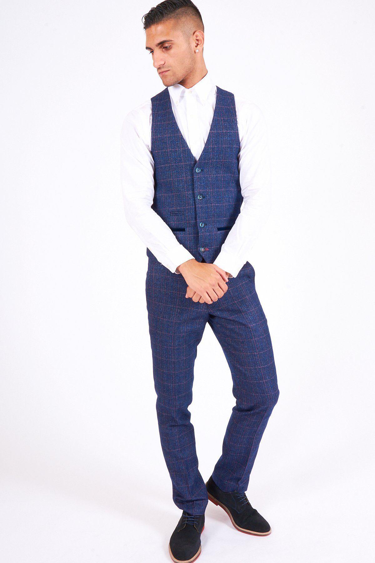 A man poses against a white background wearing marcdarcys HARRY Indigo Tweed Check Trousers, with a matching vest, white dress shirt, and black shoes—an elegant wedding ensemble. He looks down and clasps his hands in front of him.