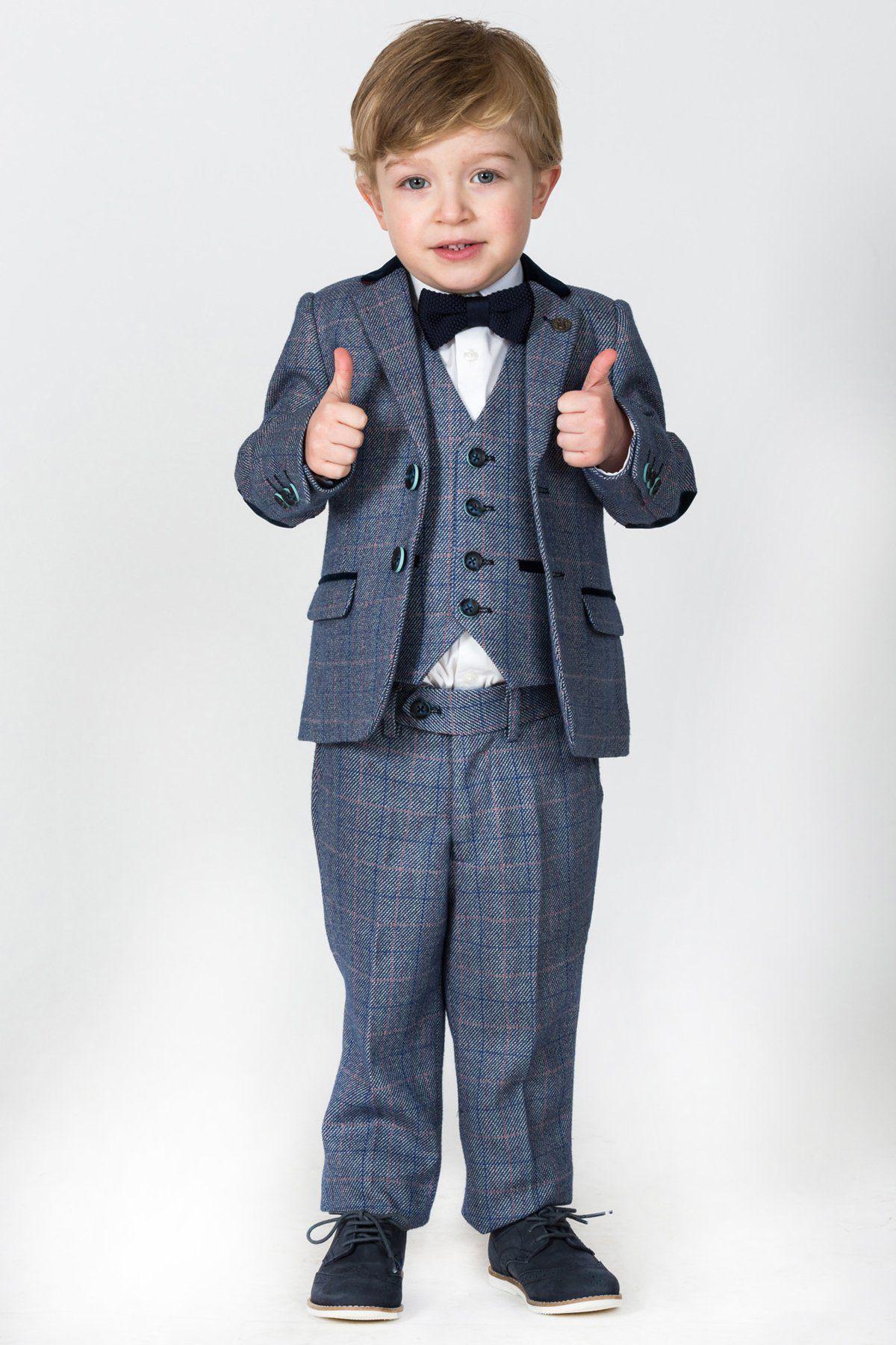 A young boy, dressed as a ring bearer in a marcdarcy HILTON Children's Blue Tweed Check Three Piece Suit with a bow tie and dress shoes, stands against a plain background, smiling and giving two thumbs up.