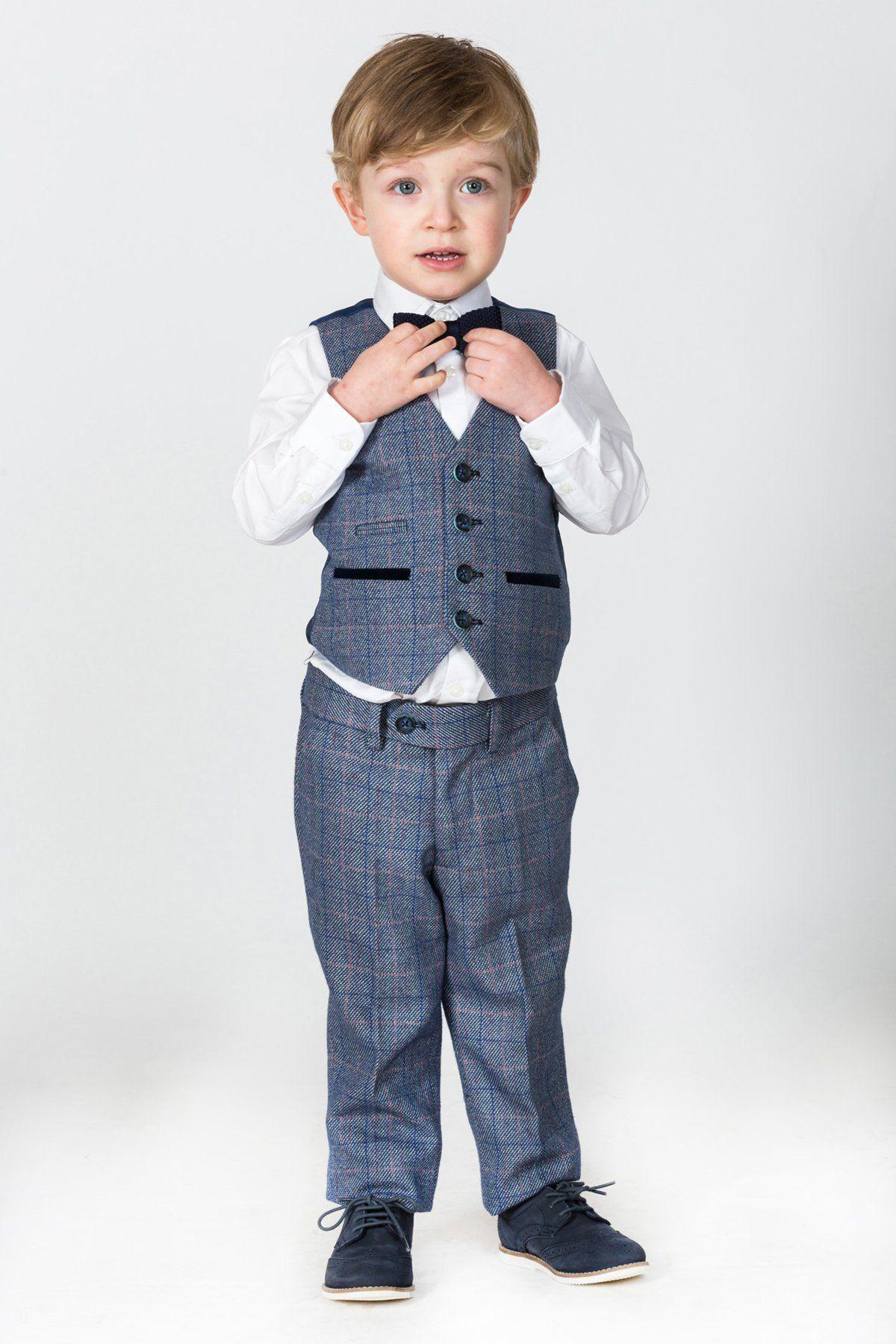 A young boy in the marcdarcy HILTON Childrens Blue Tweed Check Three Piece Suit, with a vest, white shirt, and bow tie, stands against a plain light background holding his vest and looking slightly upward.