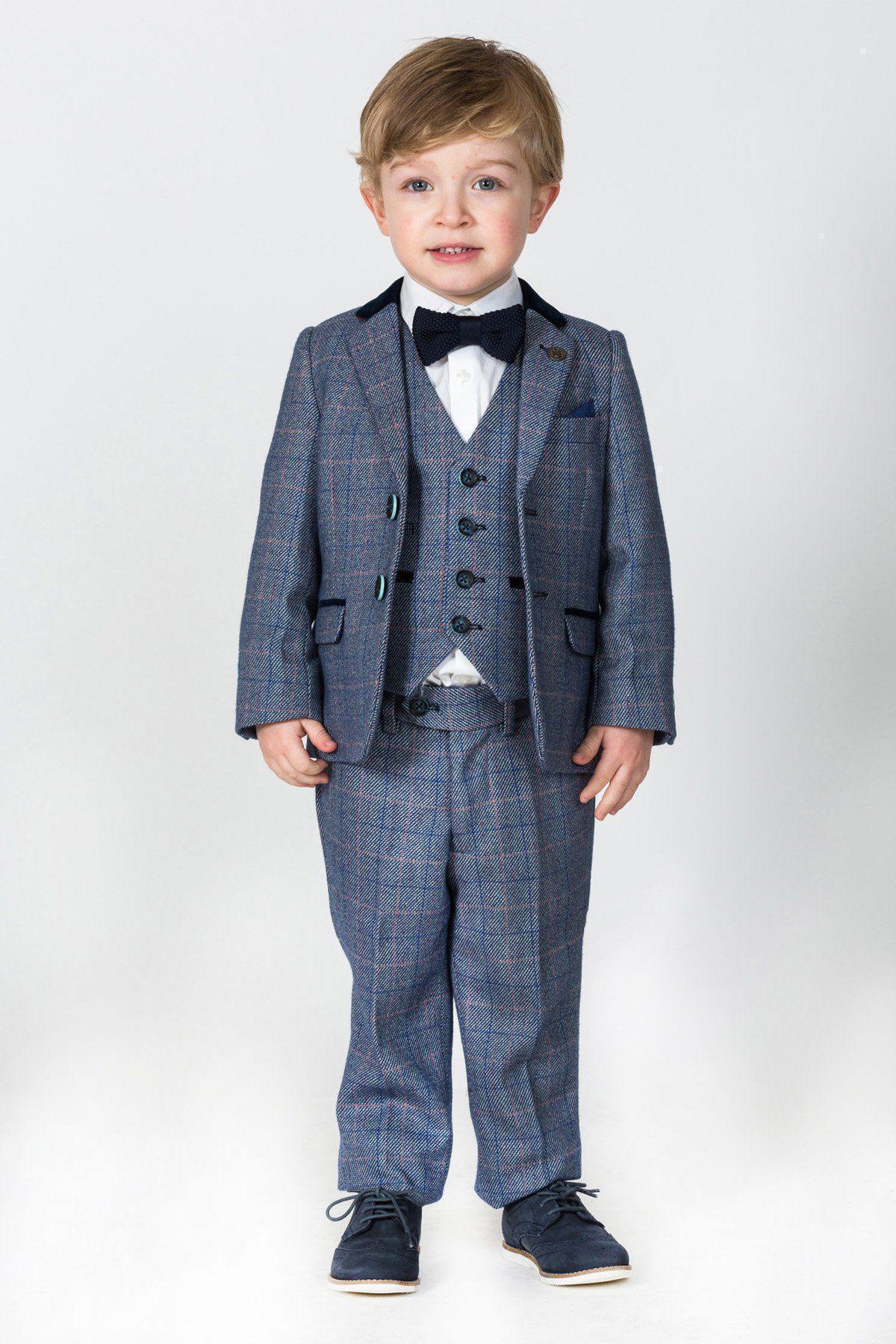 A young boy with light brown hair smiles in the marcdarcy HILTON Children’s Blue Tweed Check Three Piece Suit, paired with a white shirt and black bow tie, standing against a plain light background.