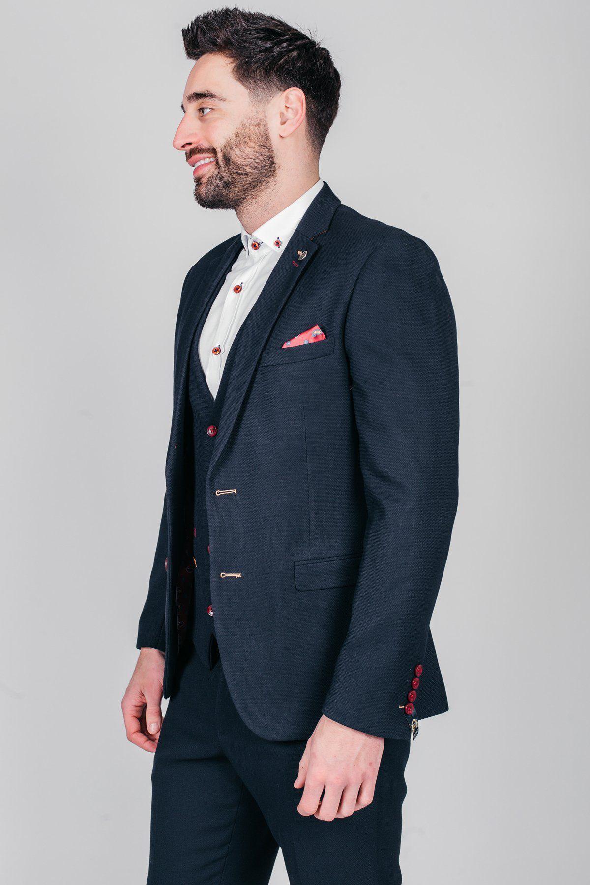 Former Sheffield United footballer Brian Deane smiles in a marcdarcy JD4 Navy Blazer, styled slim fit with a white shirt, red buttons, and pink pocket square. The background is light gray.