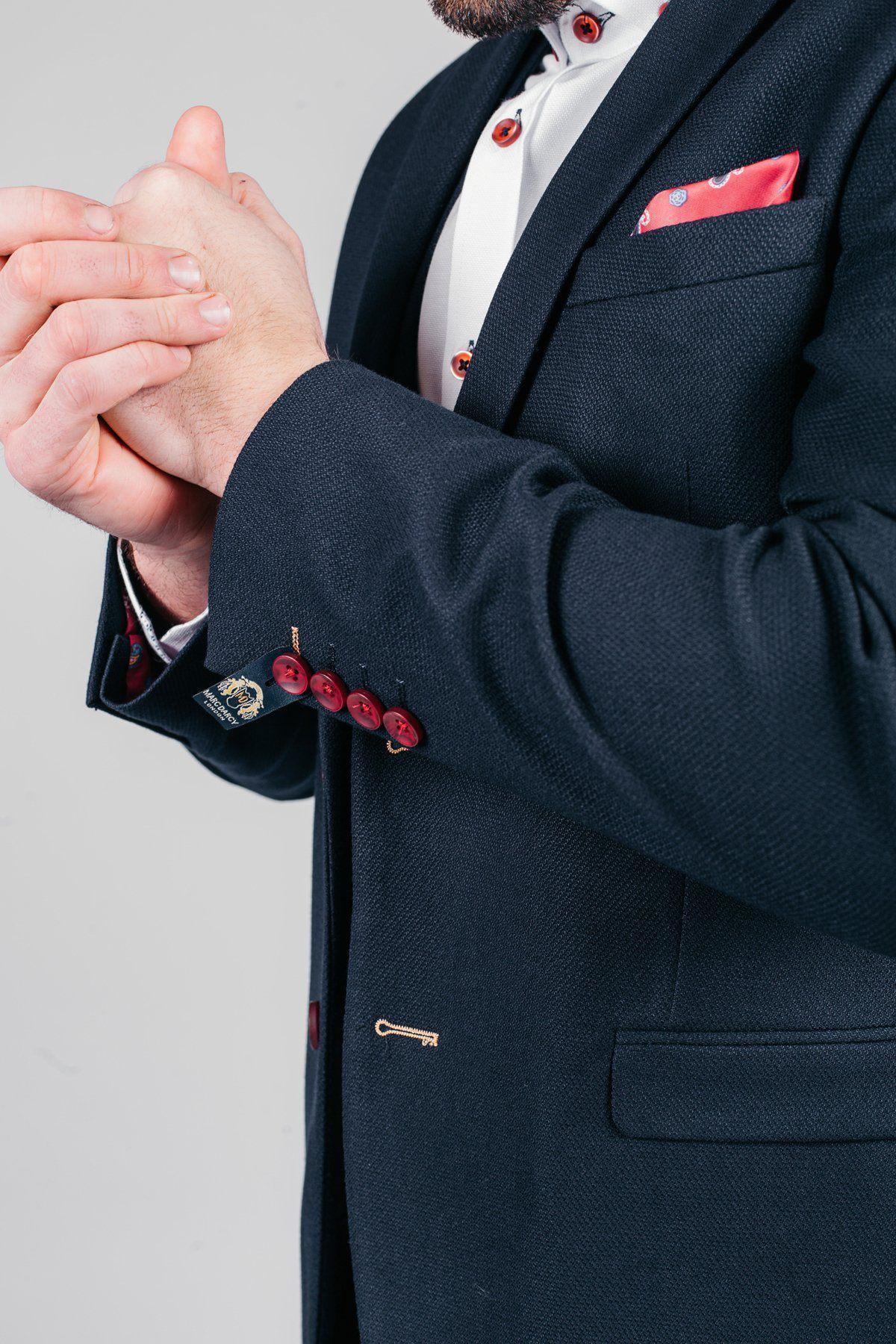 Former Sheffield United footballer Brian Deane models the marcdarcy JD4 Navy Blazer, featuring red buttons and a red pocket square over a crisp white shirt. Only his torso and hands are visible as he clasps his hands together.