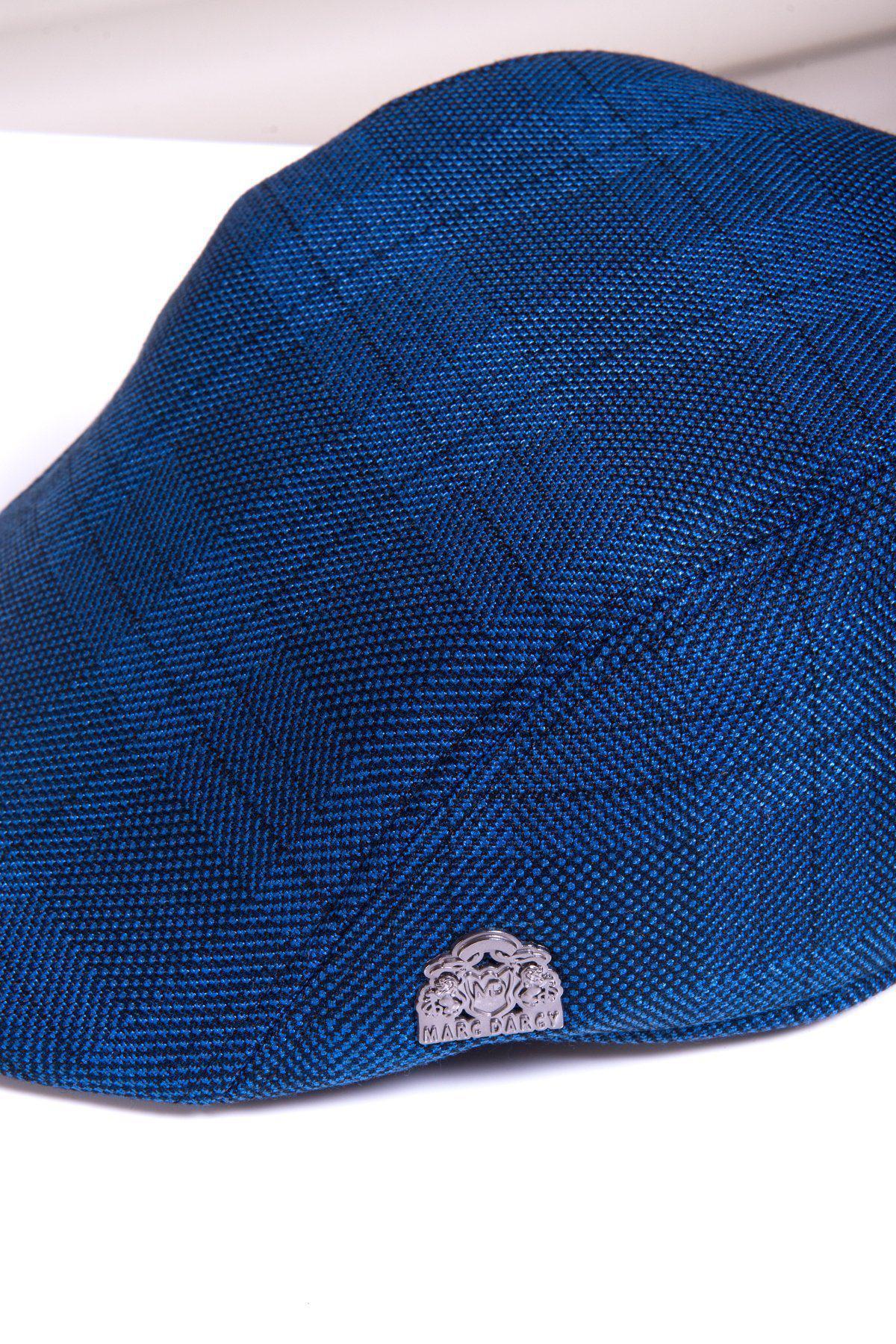 A close-up of the JERRY - Blue Check Flat Cap by Accessory, featuring textured blue fabric and a silver logo pin near the brim for a subtle vintage touch.