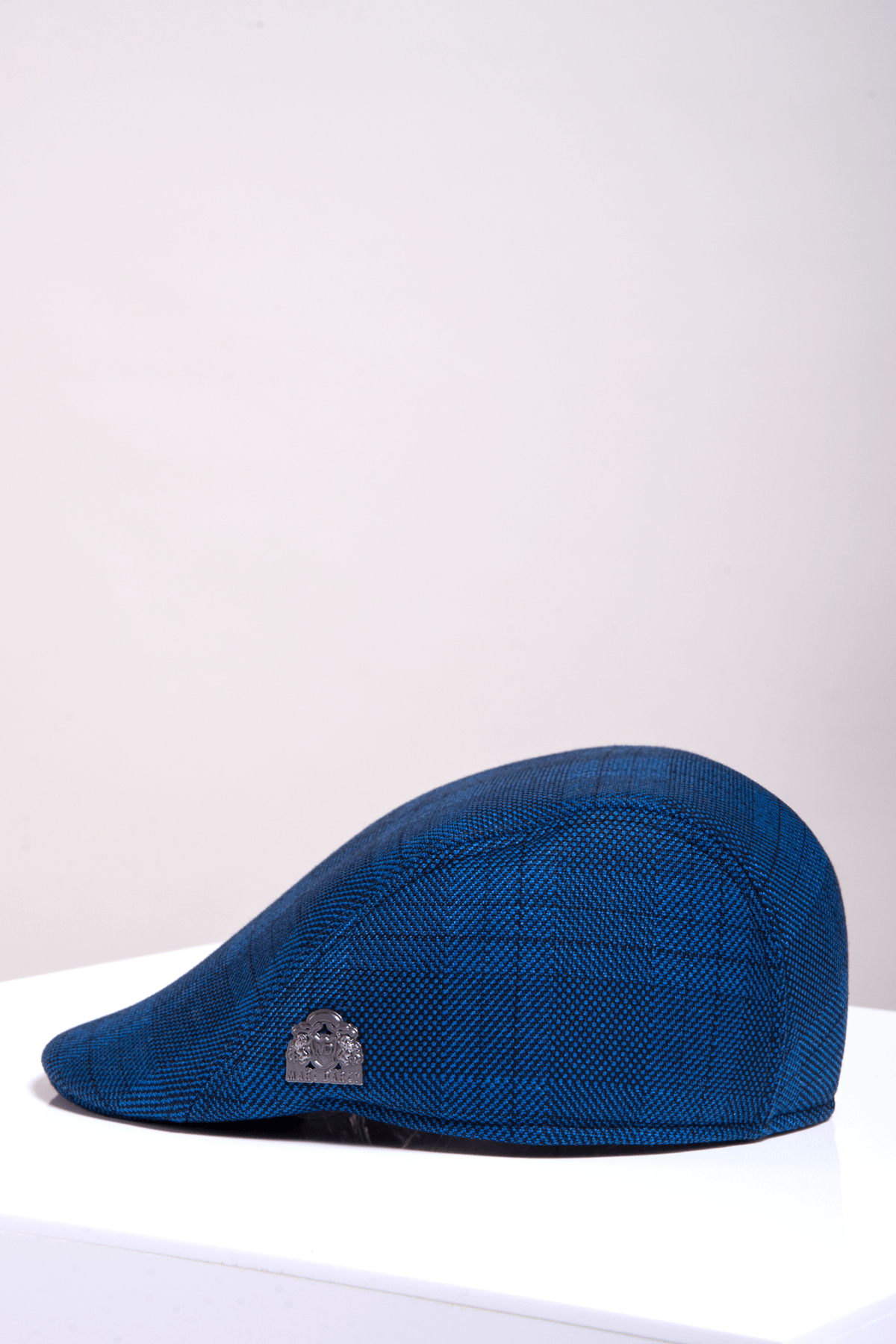 The JERRY - Blue Check Flat Cap by Accessory, featuring a subtle metallic emblem on the side, is showcased on a white surface with a light background, offering vintage charm in a style reminiscent of Marc Darcy.