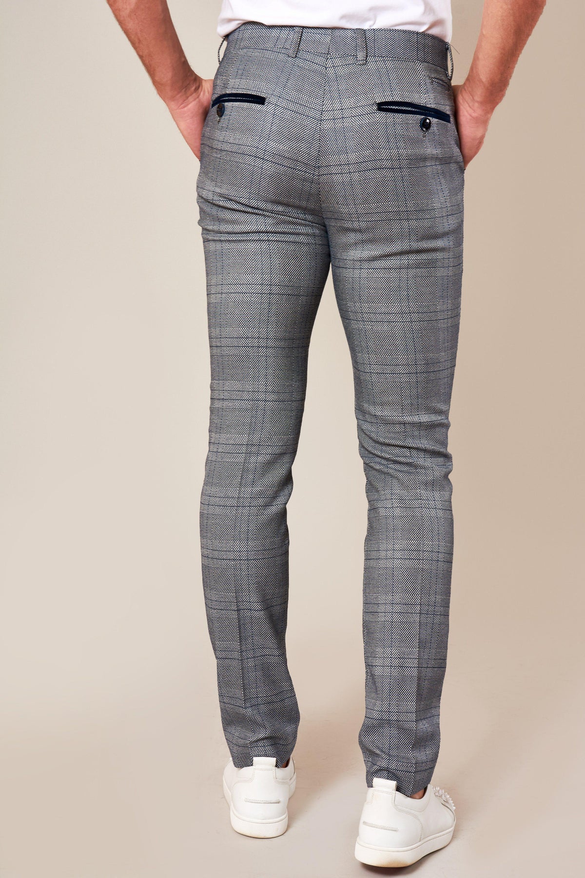 Someone stands facing away from the camera with hands in back pockets, wearing marcdarcy JERRY Skinny Fit Grey Check Trousers featuring black buttoned back pockets and paired with white sneakers.